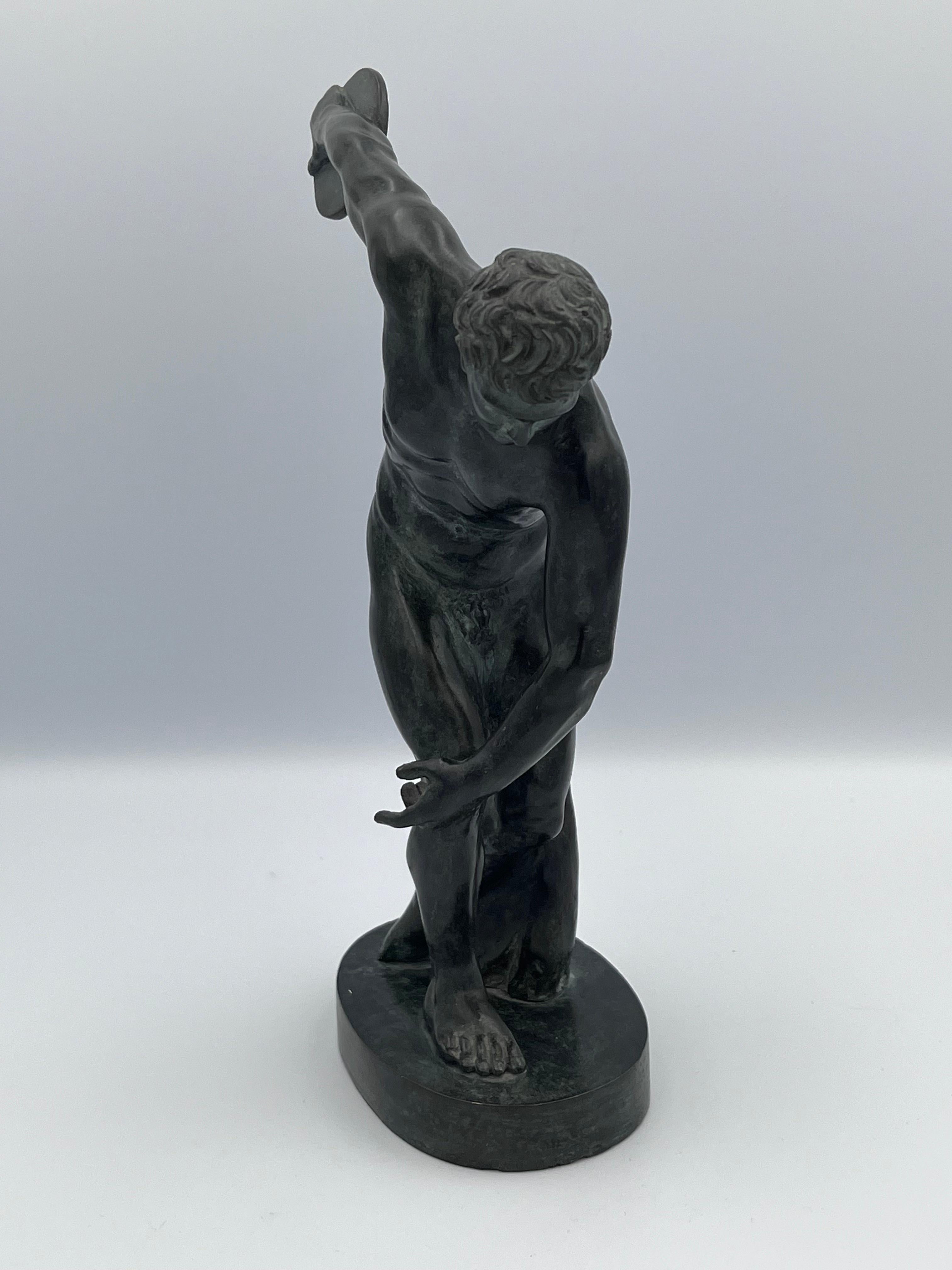 Diese Bronzeskulptur aus dem frühen 20. Jahrhundert ist eine fein gearbeitete Verkleinerung des Diskobolus von Myron, einer der berühmtesten Skulpturen des klassischen Altertums. Mit einer Größe von ca. 10 Zoll fängt sie die dynamische Energie und