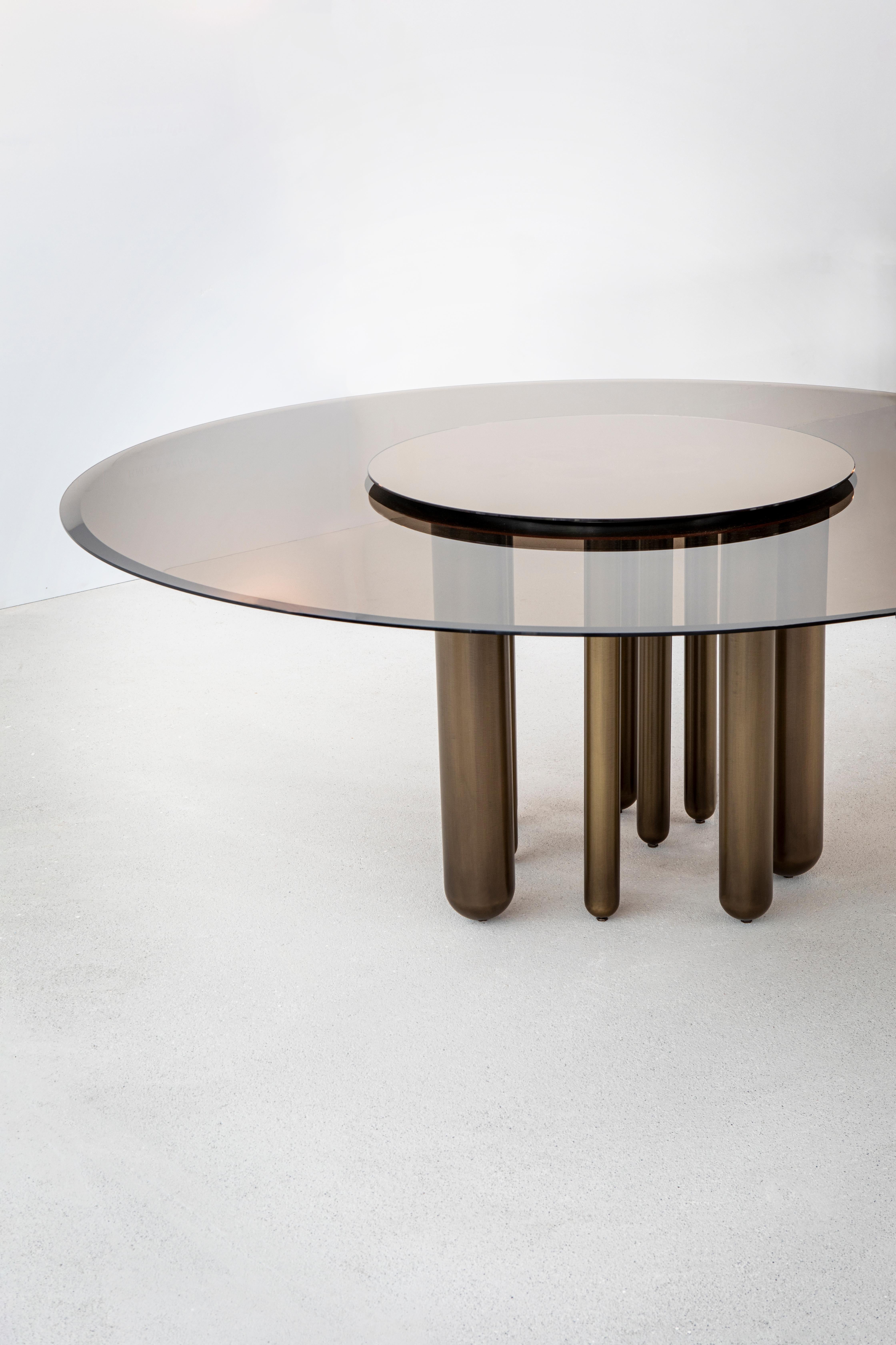 A transparent bronze glass top and mirrored Lazy Susan are supported on a base of irregularly spaced brass legs of different sizes. A chord. A beat. A rhythm. A glimmering bronze finish and sparkling mirror, always shining, always spinning, this