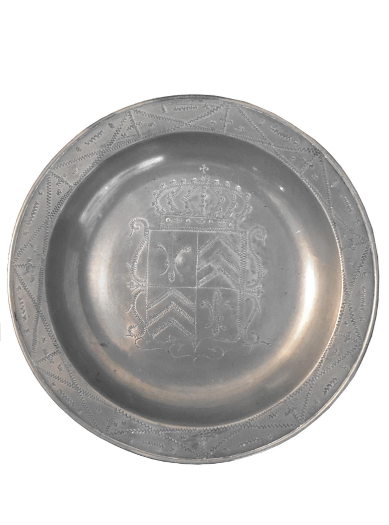 Pewter deep dish with crowned coat of arms with fleur de lys and Chevrons in the center. The
crown topped by a cross is possibly ducal. Chiseled rim. There is a crowned mark almost
obliterated by use on the back of the dish.
Origin: