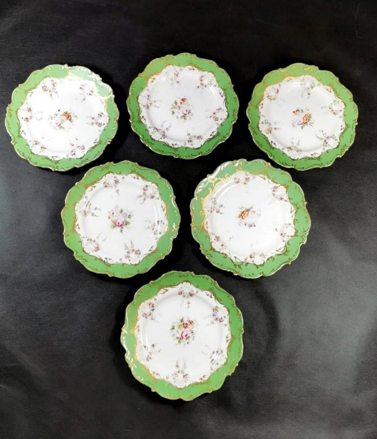 Six antique French porcelain dishes; they have a softly shaped shape; the refined Baroque decorations that delimit the green border are in pure gold; along the inner border and in the center there are elaborate multicolored floral shoots, one