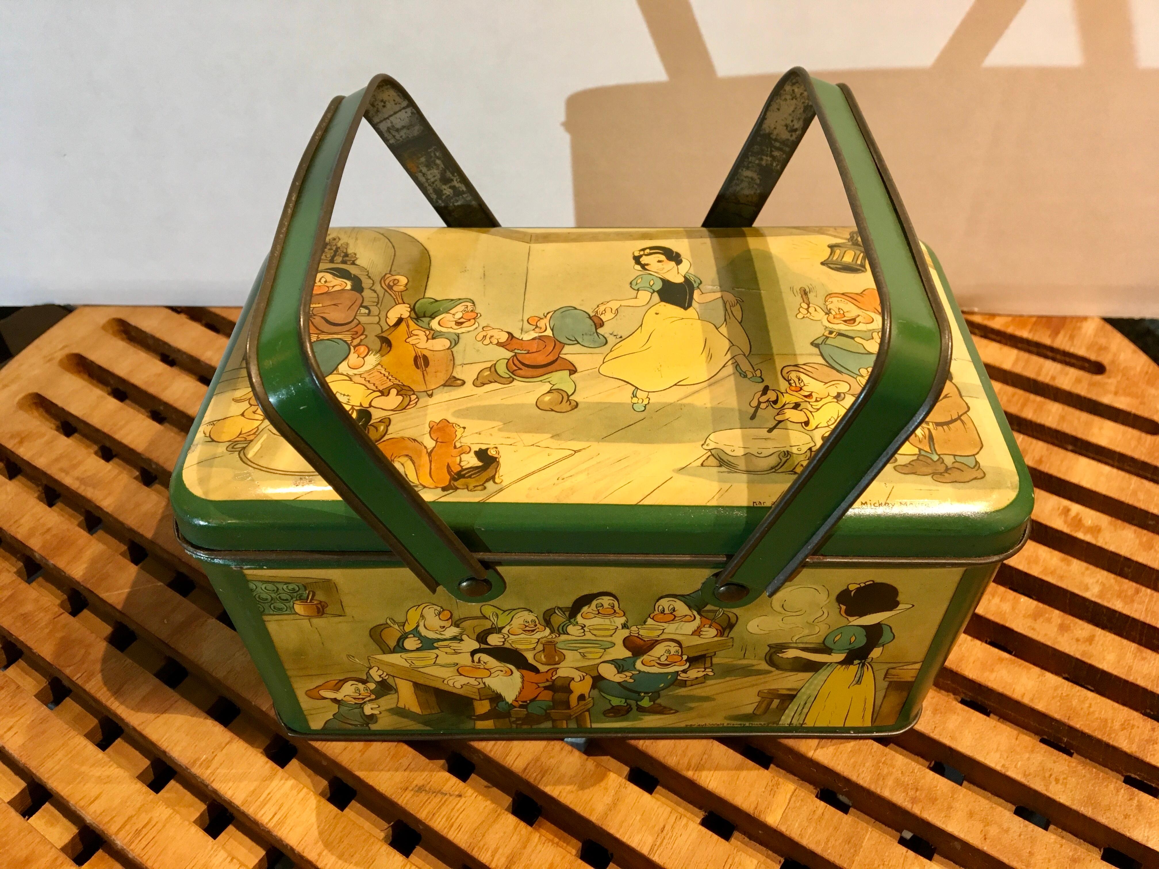 Disney tin with handle with Snow White and the 7 dwarfs. 
A green rectangular tin with lid with different scenes of Snow White , the seven dwarfs and the Prince on his white horse.
Made under licence of Walt Disney for the European market. 
Marked