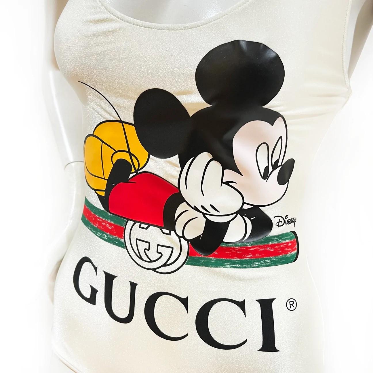 One-Piece Swimsuit by Disney X Gucci
Spring/Summer 2020
Made in Italy
Ivory 
Mickey Mouse Gucci logo graphic on front
Criss-cross back straps   
Fabric Composition; 80% polyamide, 20% elastane
New With Tags (still includes protective