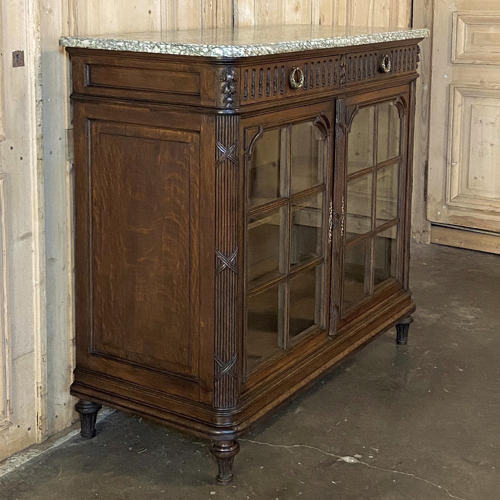 19th century French Louis XVI marble top display buffet was handcrafted from solid old-growth oak and given a walnut color, and features fluted and reeded adornment on the drawer facades, centered with cast bronze wreath pulls. The corners are