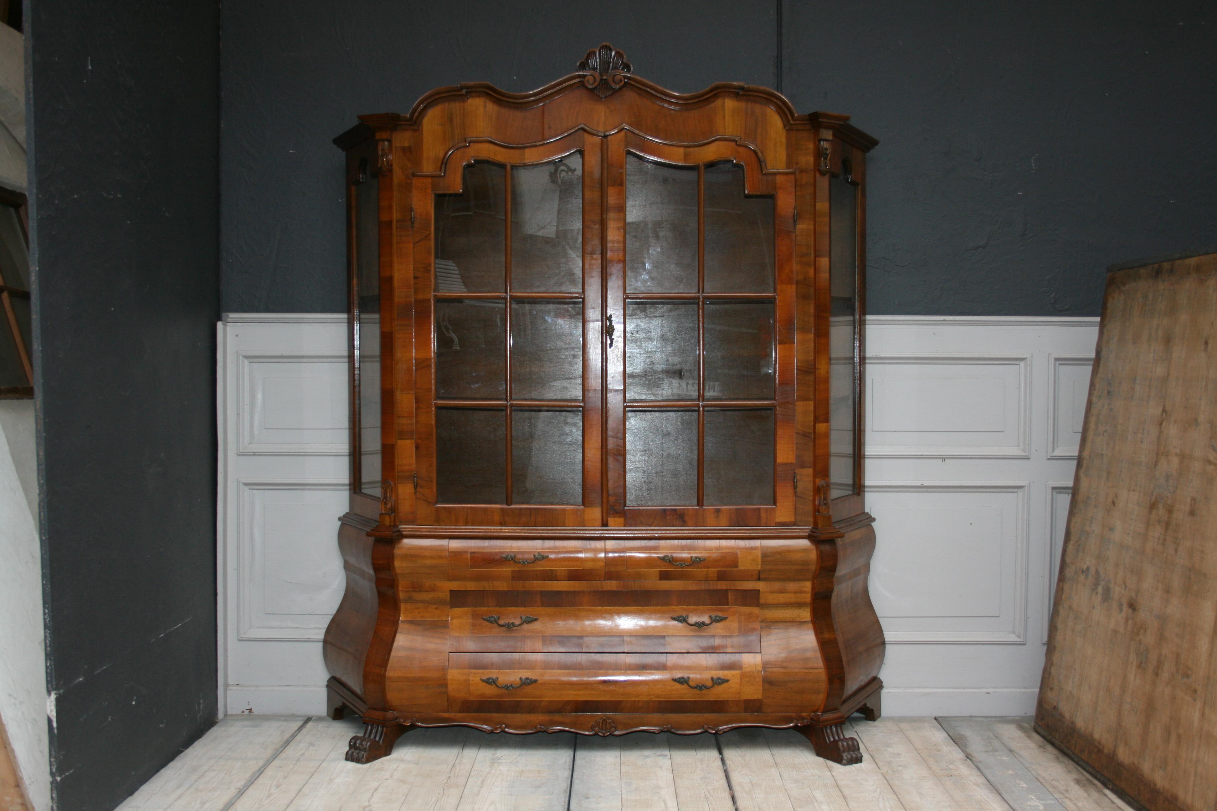 Large 20th century display cabinet in Dutch Baroque style with walnut veneer on a strongly bowed frame. Probably made in Italy. The display cabinet consists of a bulging base (Pedestal on claw-feet) with 2 large drawers and 2 small drawers, and a