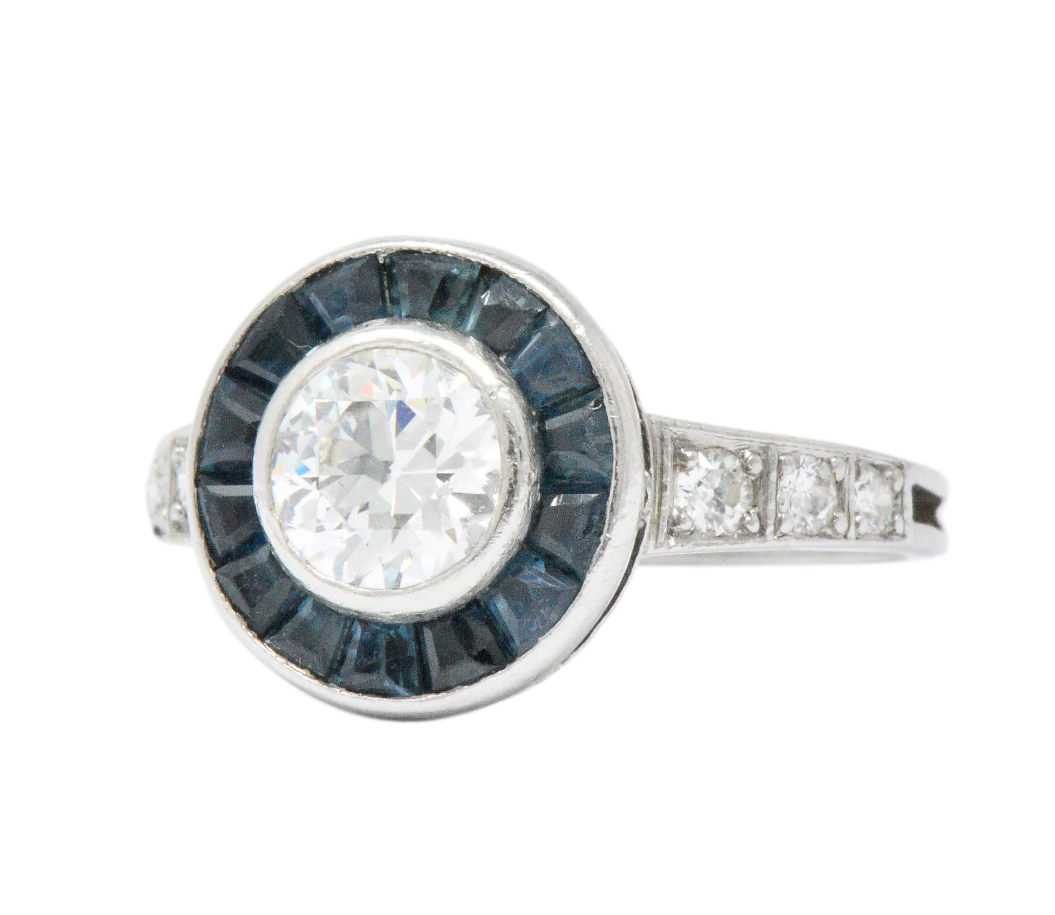 Centering an old European cut diamond weighing approximately 0.55 carats, G color and VS clarity

With a calibré cut sapphire surround, deep blue 

Old European cut diamonds accenting the shank and weighing approximately 0.12 carats total, eye-clean