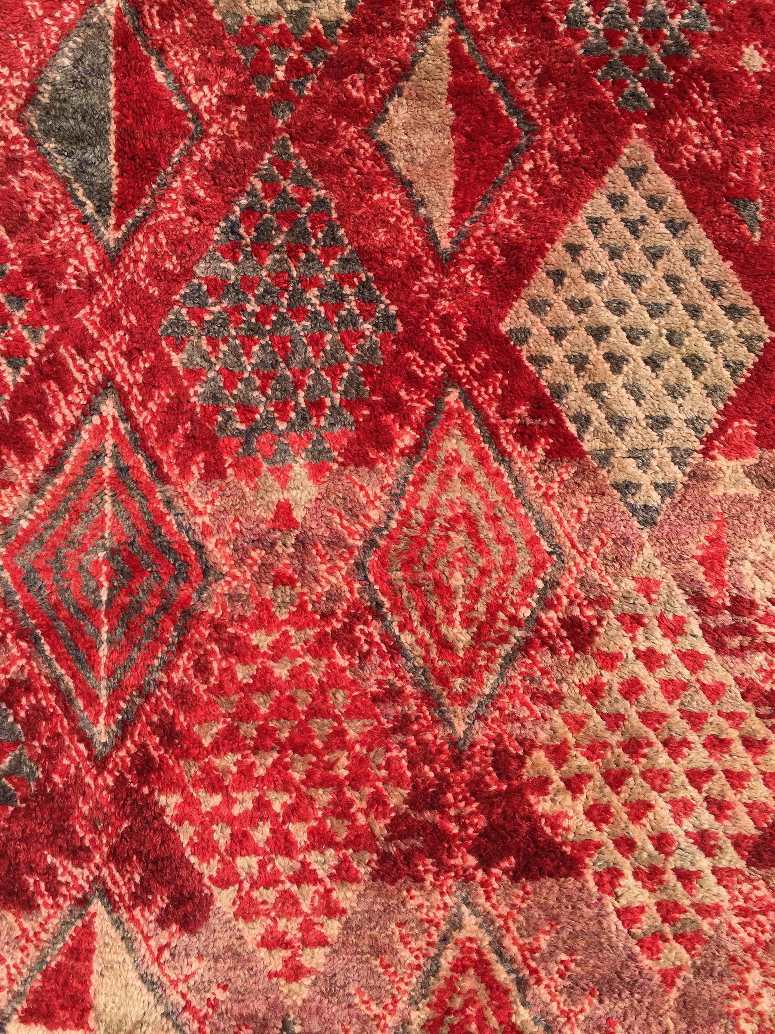Questo tappeto, un coloratissimo esempio di Beni M'Guild, presenta un forte messaggio berbero nei toni del rosso e del lavanda con accenti di grigio antracite. Le losanghe sono bilanciate in modo ponderato sul campo, alcune riempite con forme a
