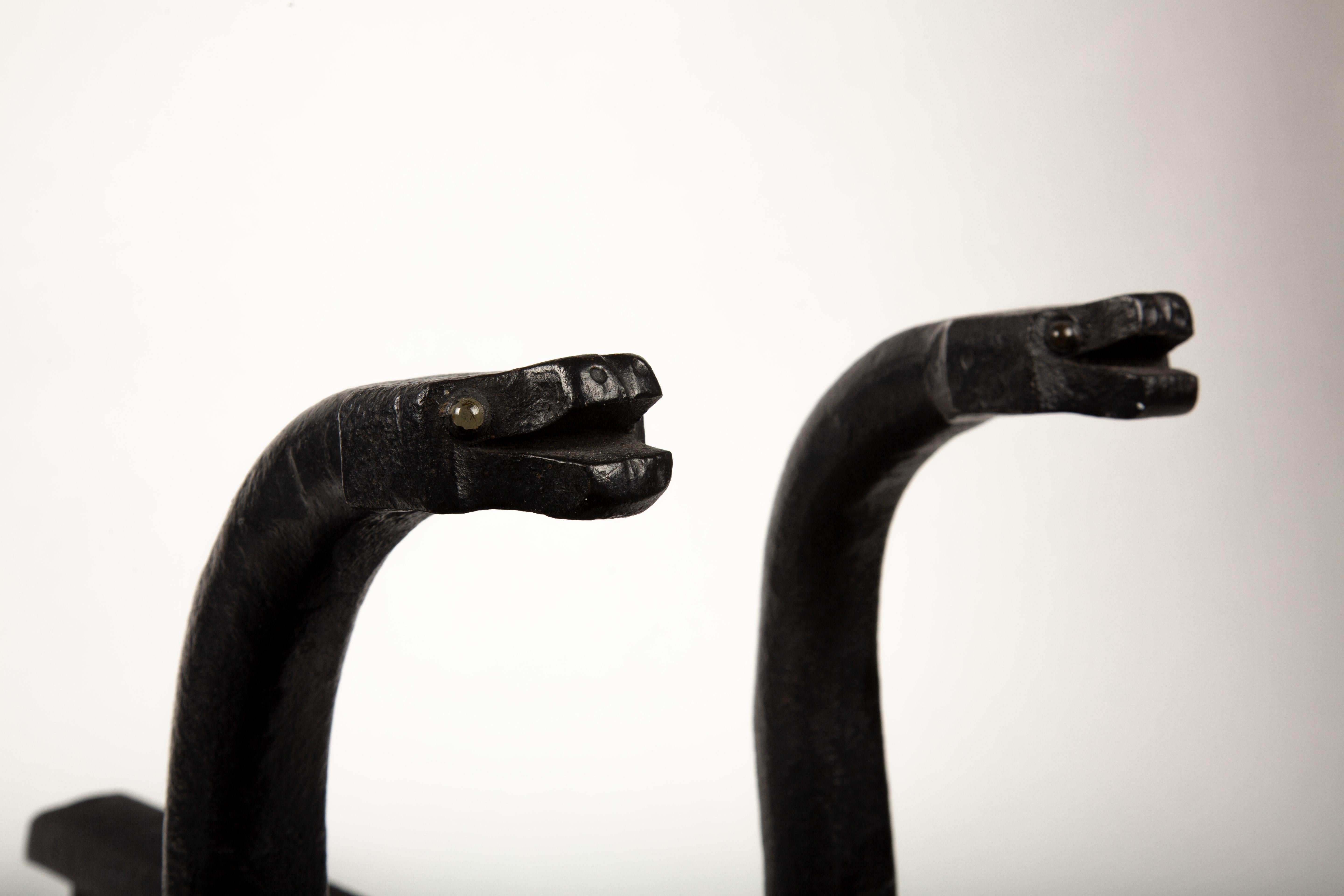 Wunderschönes Paar antiker Folk Art Schlangen-Andirons mit eingelassenen Glasaugen. Sie wurden von Schmieden aus handgehämmertem Schmiedeeisen hergestellt. Der Künstler benutzte Stücke von Eisenbahnschienen, um ein einzigartiges Set von schweren,