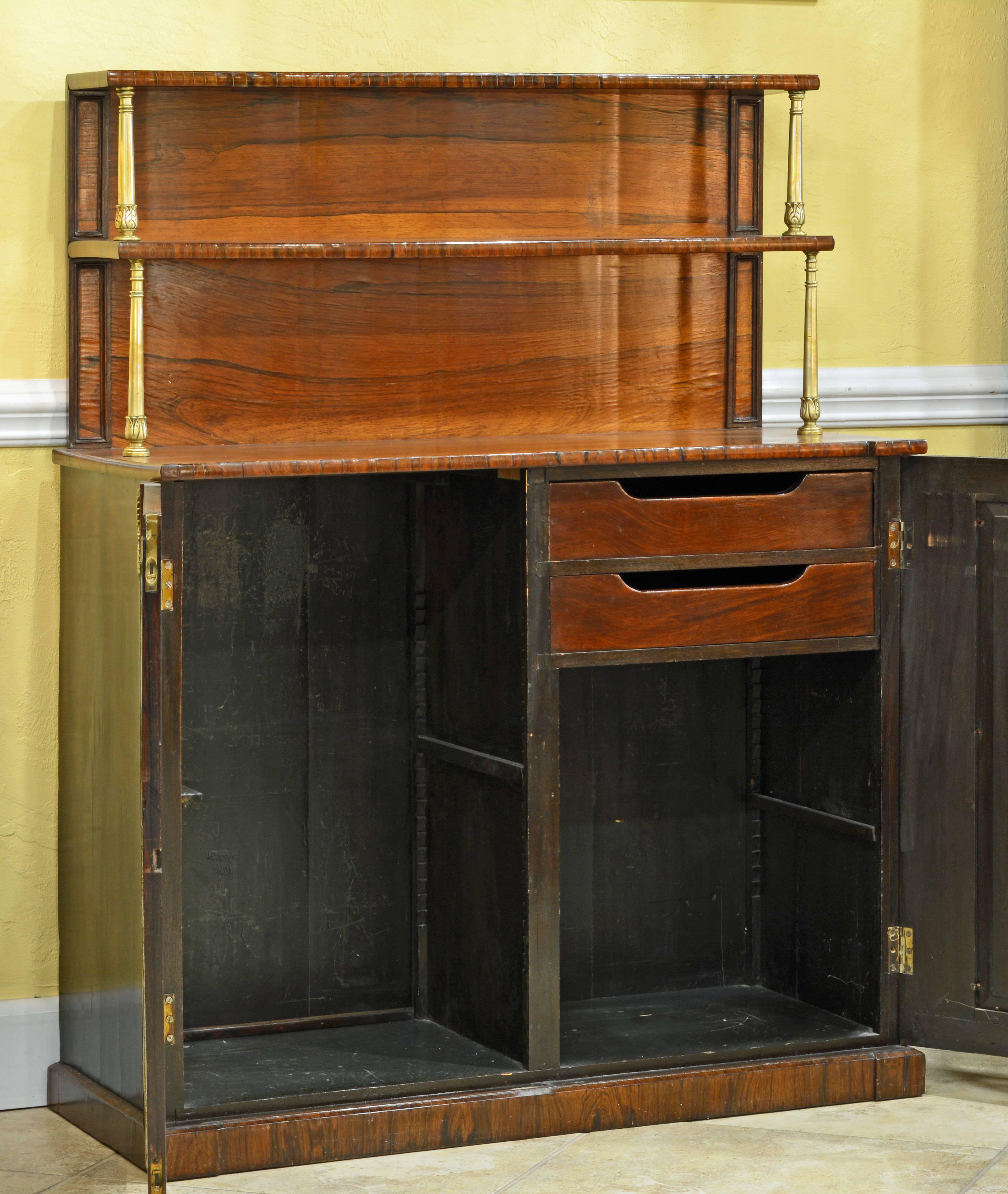 This noble piece of furniture in superb quality rosewood features two raised shelves supported by archantus themed brass columns above the lower section resting on a plinth base and with two paneled and brass trimmed doors flanked by bronze mounts