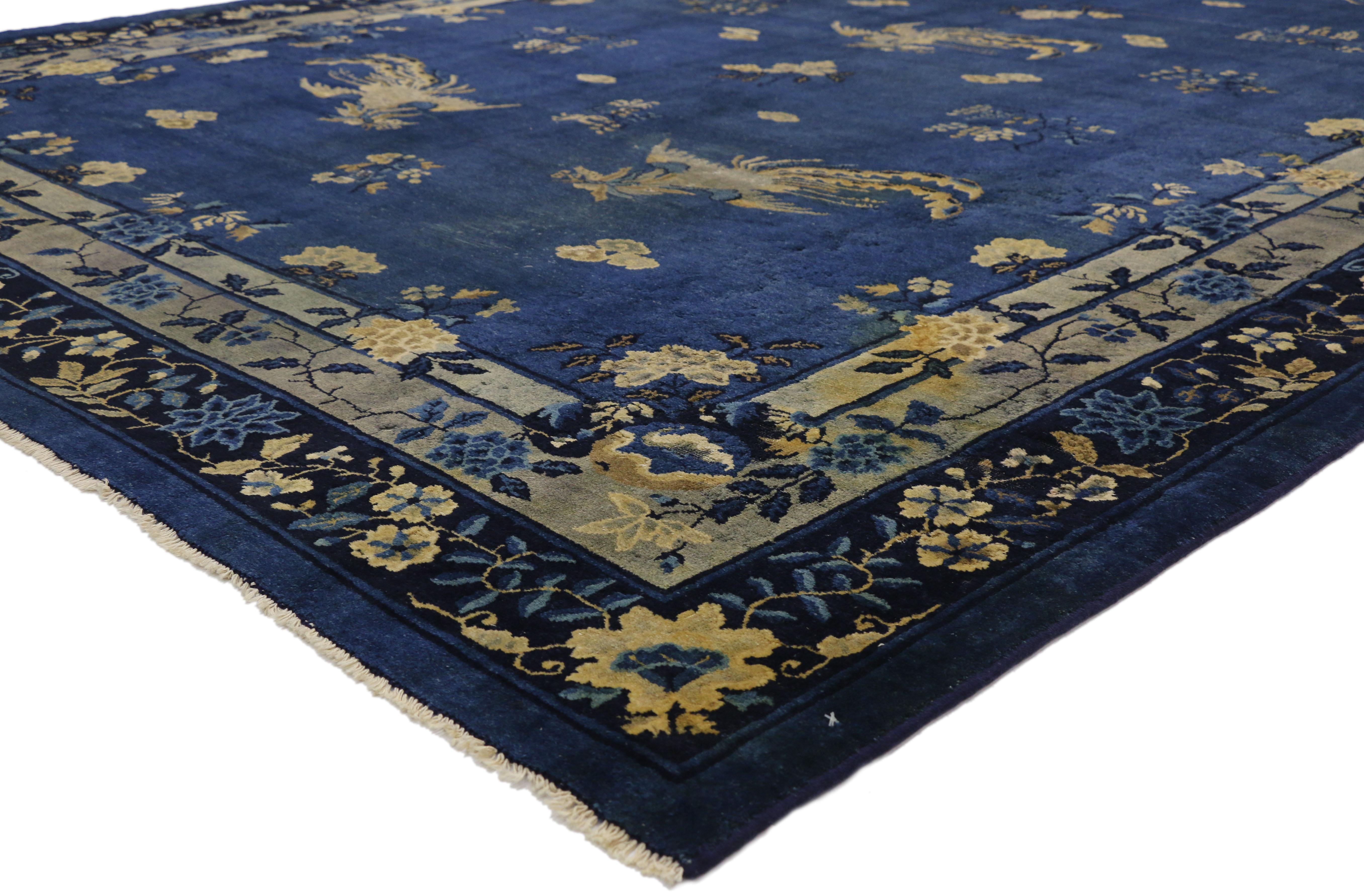 77266 distressed Antique Chinese Peking rug with Traditional Chinoiserie style. This distressed hand knotted wool antique Chinese Peking rug features a variety of phoenix and floral motifs spread across an abrashed blue field. Five large phoenixes,