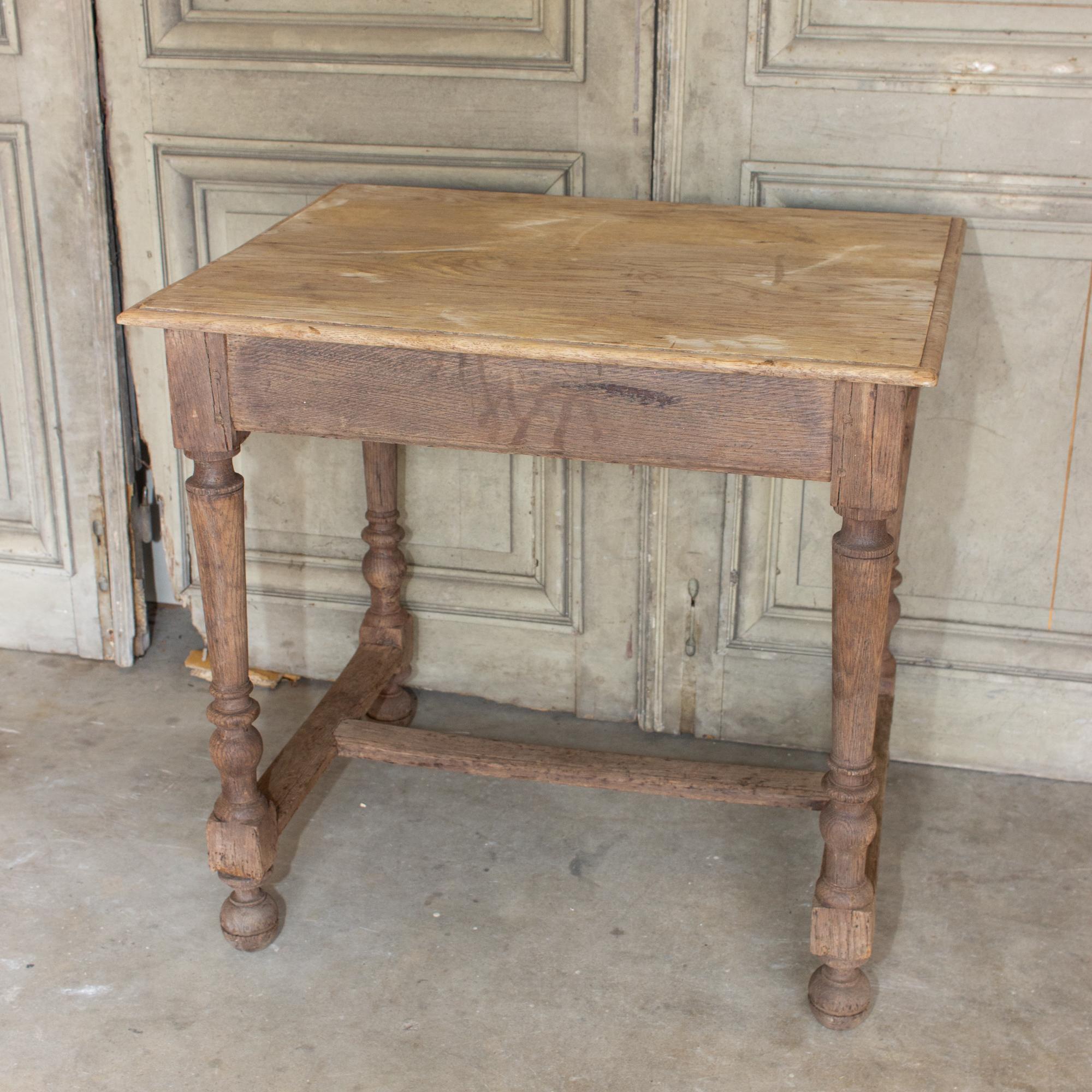 This antique French oak side table has a distressed finish with patination present, giving it a weathered and well-loved look. The legs feature turned details and a stretcher-style base with round, ball-feet. There is no storage in the table, but