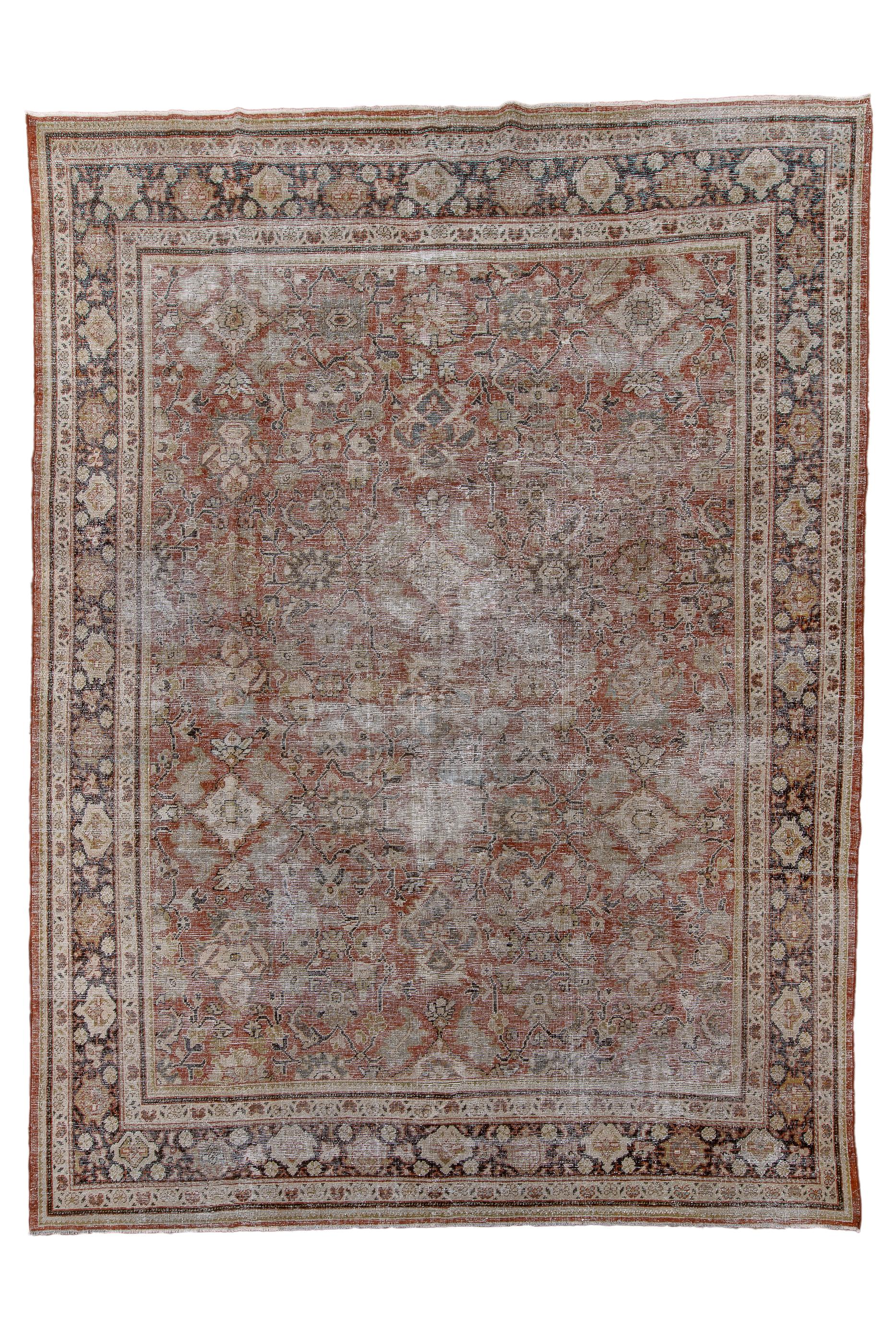 This spot-distressed room size carpet shows a mellow tomato madder field with an allover array of various lozenge-form, quasi-floral elements in shades of cream, straw and  very small bits of dark blue. Chocolate main strip style border with