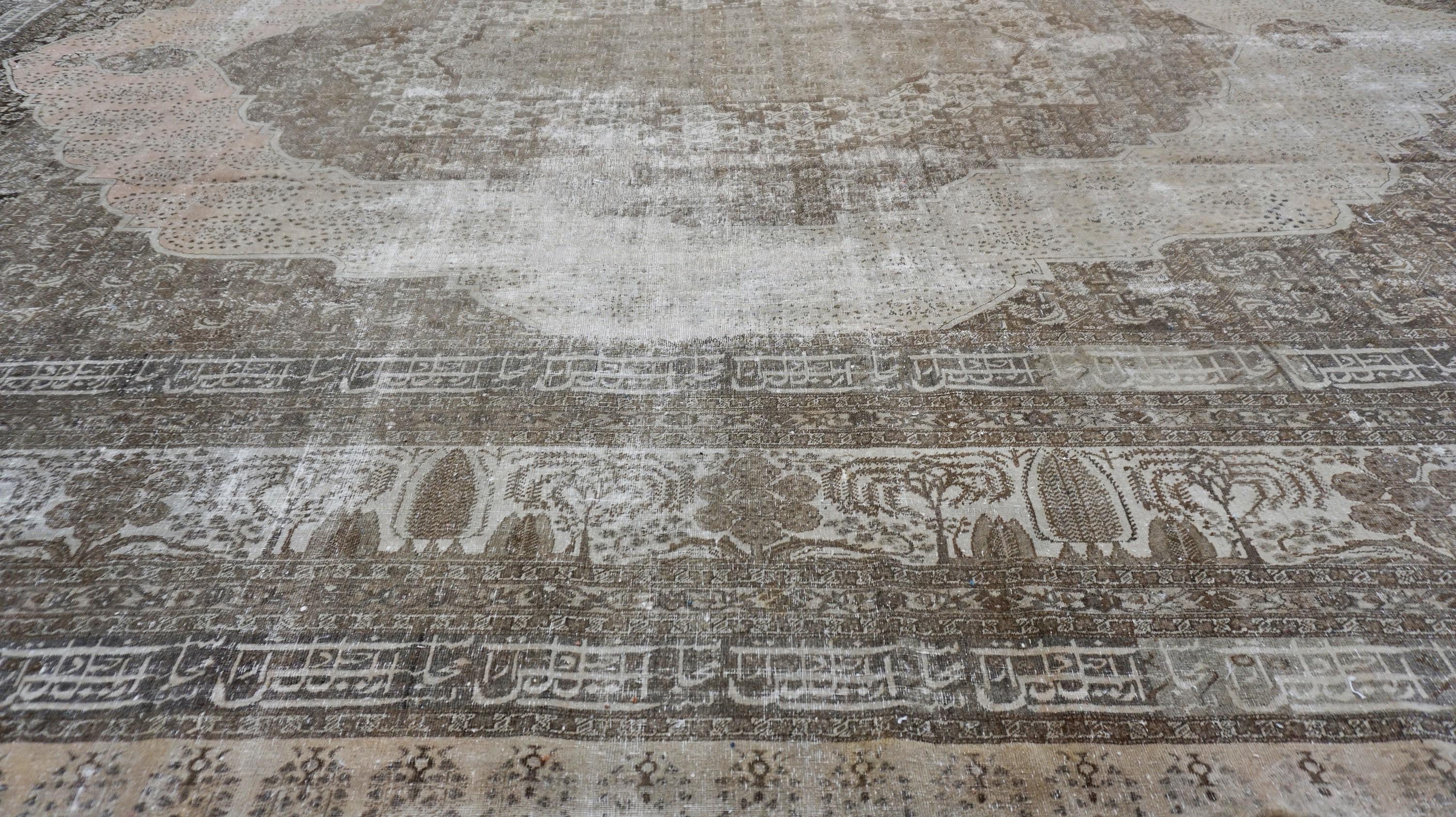 This antique hand-knotted wool rug is a majestic example of traditional Mohtasham-style artistry, distinguished by its grand scale and time-softened palette. The rug features a majestic central medallion framed by intricately detailed floral motifs
