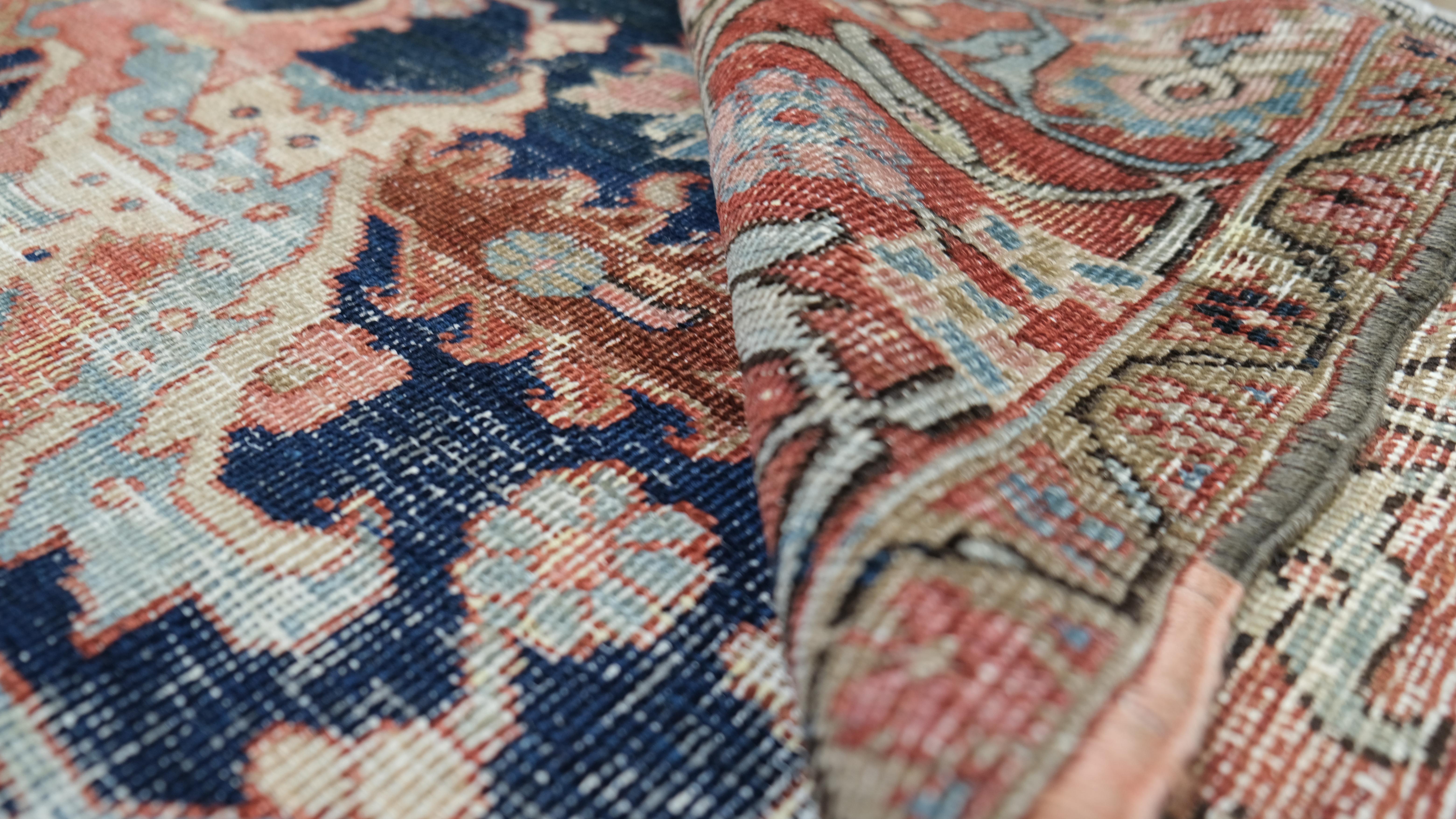 Dieser exquisite antike, handgeknüpfte Wollteppich zeigt in seiner Mitte ein großes Blumenmedaillon, das von komplizierten, von der Natur inspirierten Motiven umgeben ist. Das satte marineblaue Feld bildet den perfekten Hintergrund für die zartrosa,