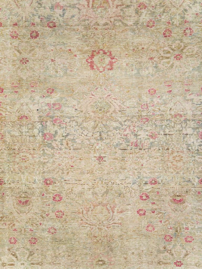 An antique Persian Lavar Kerman carpet from the early 20th century with an intricate floral pattern that has been subdued. Overall beige, this carpet has secondary tones in green, pink, and blue.