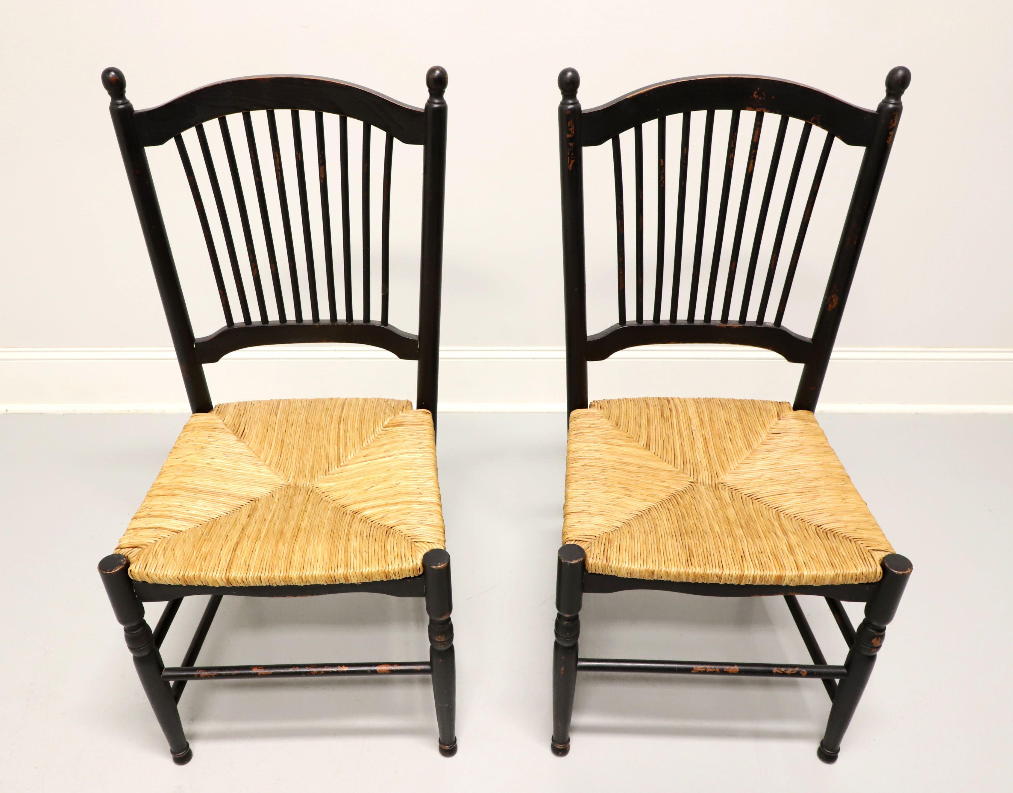 A pair of dining side chairs in the Cottage / Rustic style, unbranded. Solid hardwood painted black, distressed with touches of red, arched crest rail with spindle backs, rounded stiles capped with finial posts, rush seats, carved apron, turned