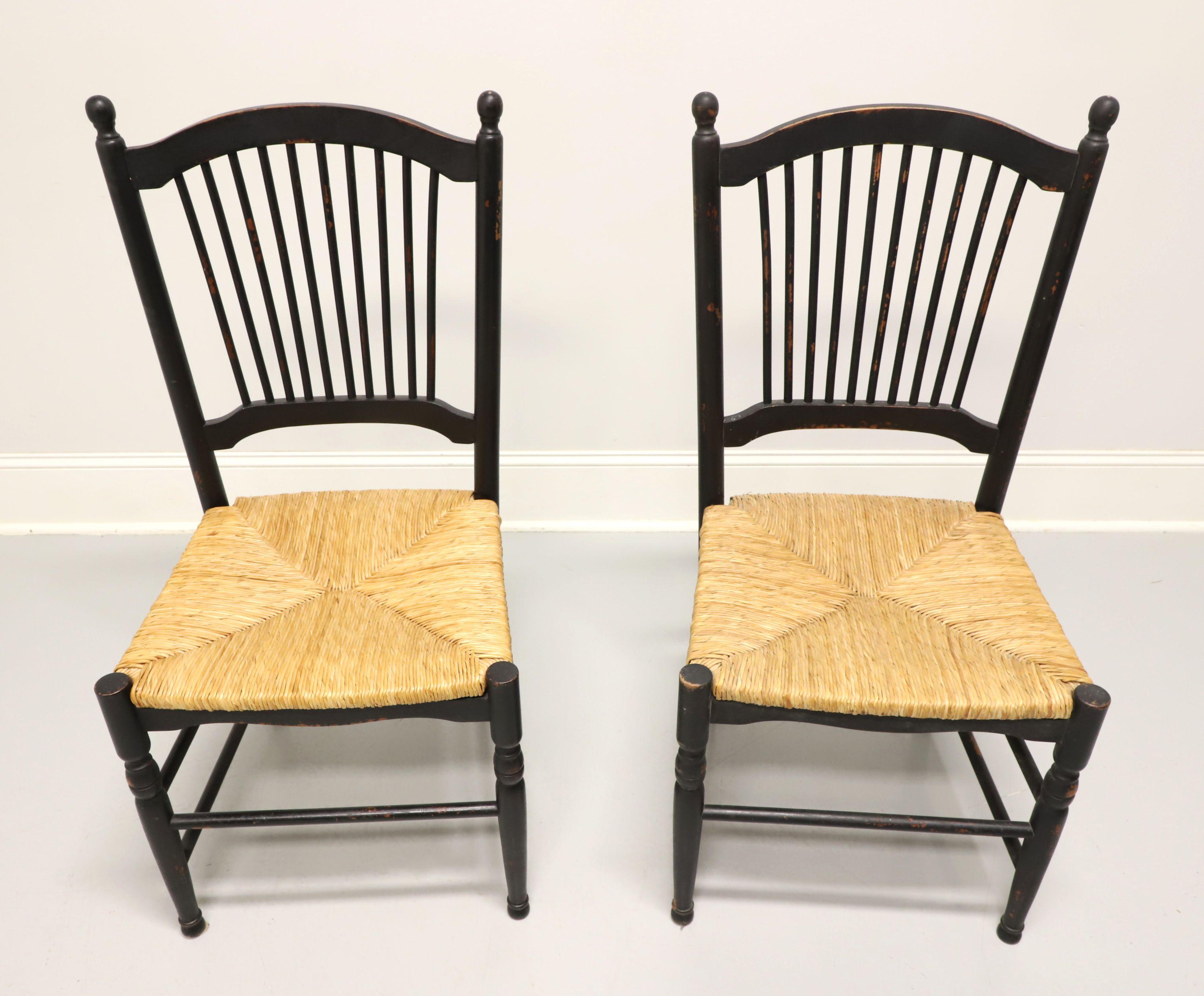 A pair of dining side chairs in the Cottage / Rustic style, unbranded. Solid hardwood painted black, distressed with touches of red, arched crest rail with spindle backs, rounded stiles capped with finial posts, rush seats, carved apron, turned