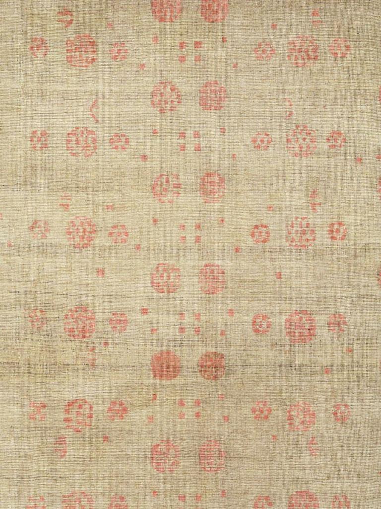 An antique East Turkestan distressed Khotan carpet in gallery size format from the early 20th century. The beige field of this Xinjiang province (western China) oasis town rug displays two columns of the characteristic vase and pomegranate tree