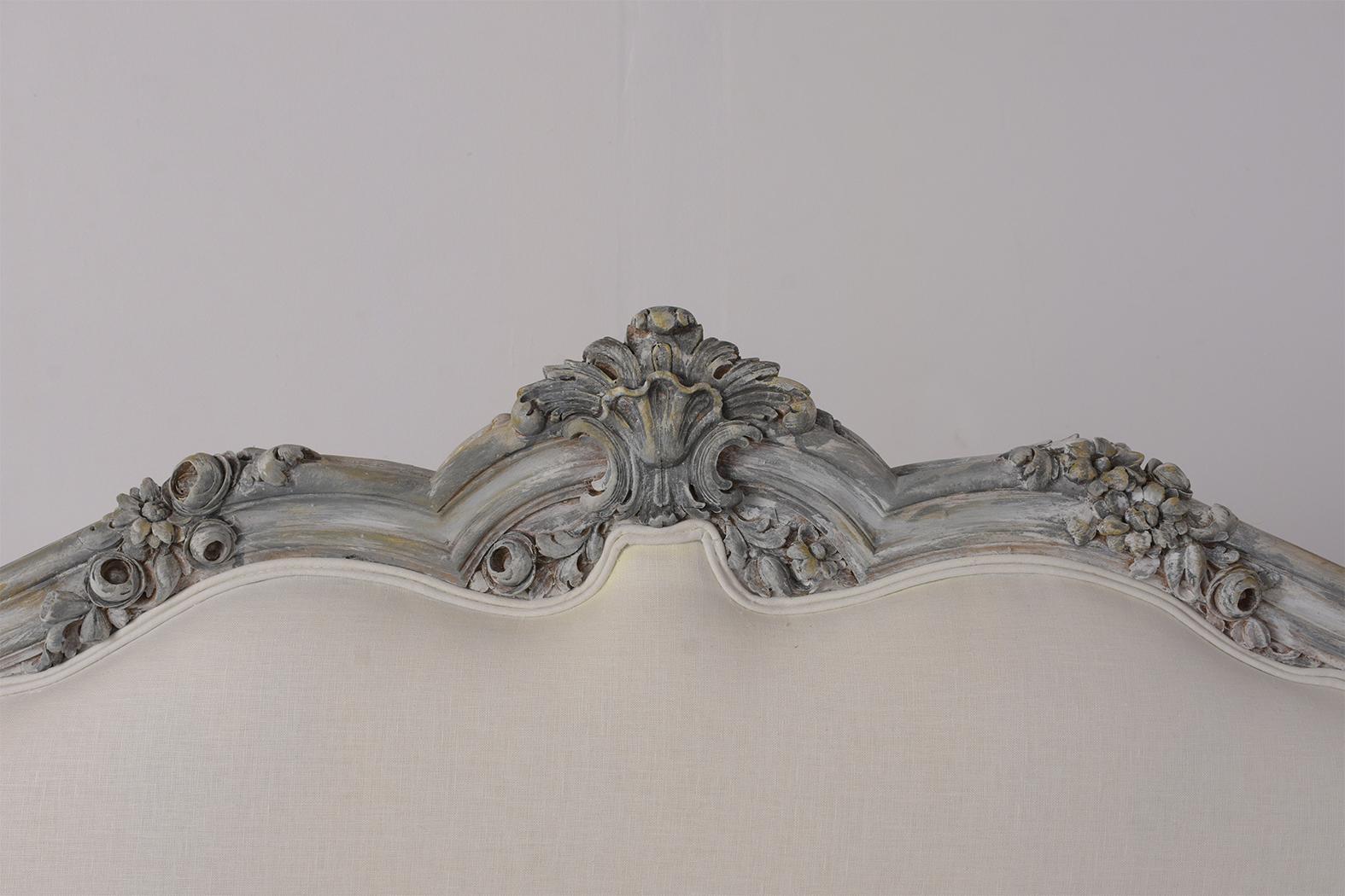 This Italian Louis XV style queen size bed frame features a wood frame painted in a pale grey and off the white color combination with a distressed finish. There are detailed carvings of flowers, leaves, garland, and seashells all along the