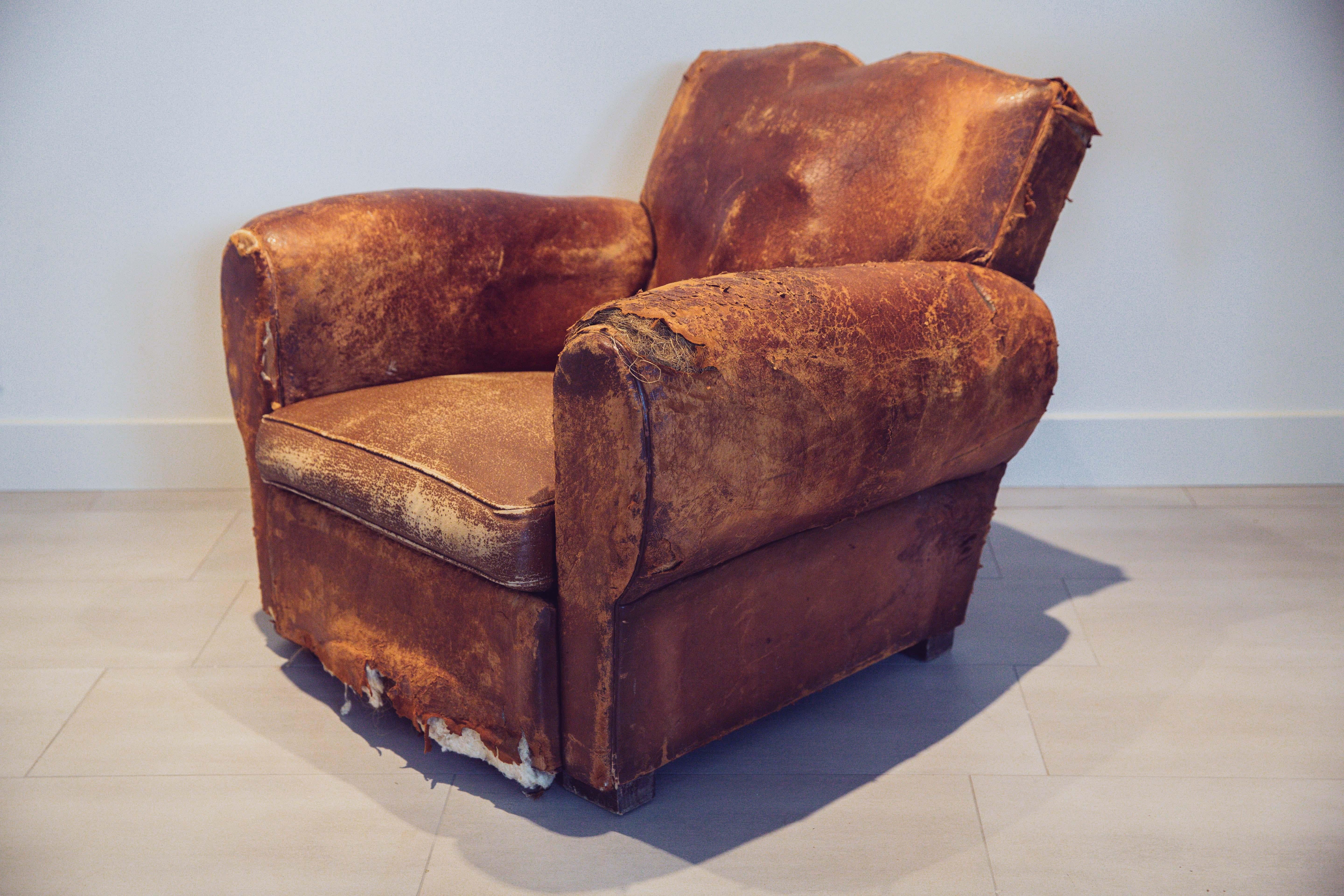 Heavily distressed French Art Deco club chair. Upholstered in a cognac leather, features a distinctive French mustache seat back and large balloon arms. In original condition with great wear. Could be a restoration project, or just leave it the way
