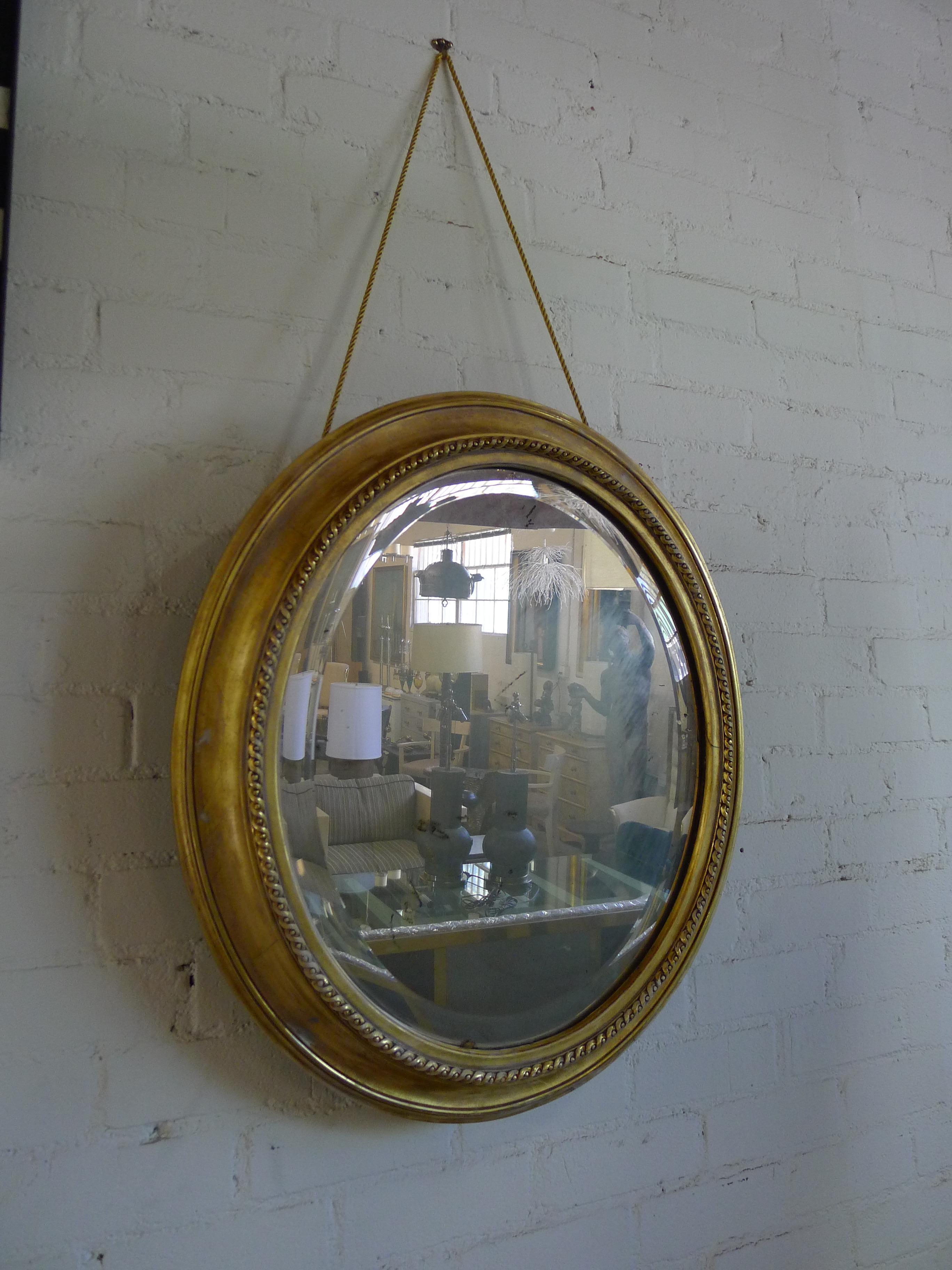 Oval gilded mirror in a classic antique style, with new distressing, new rope and new 22K gold finishes for the frame. Mirror is antiqued see all imaging. Hung by rope.

The wood frame has age marks and cracklature throughout, indicative of the