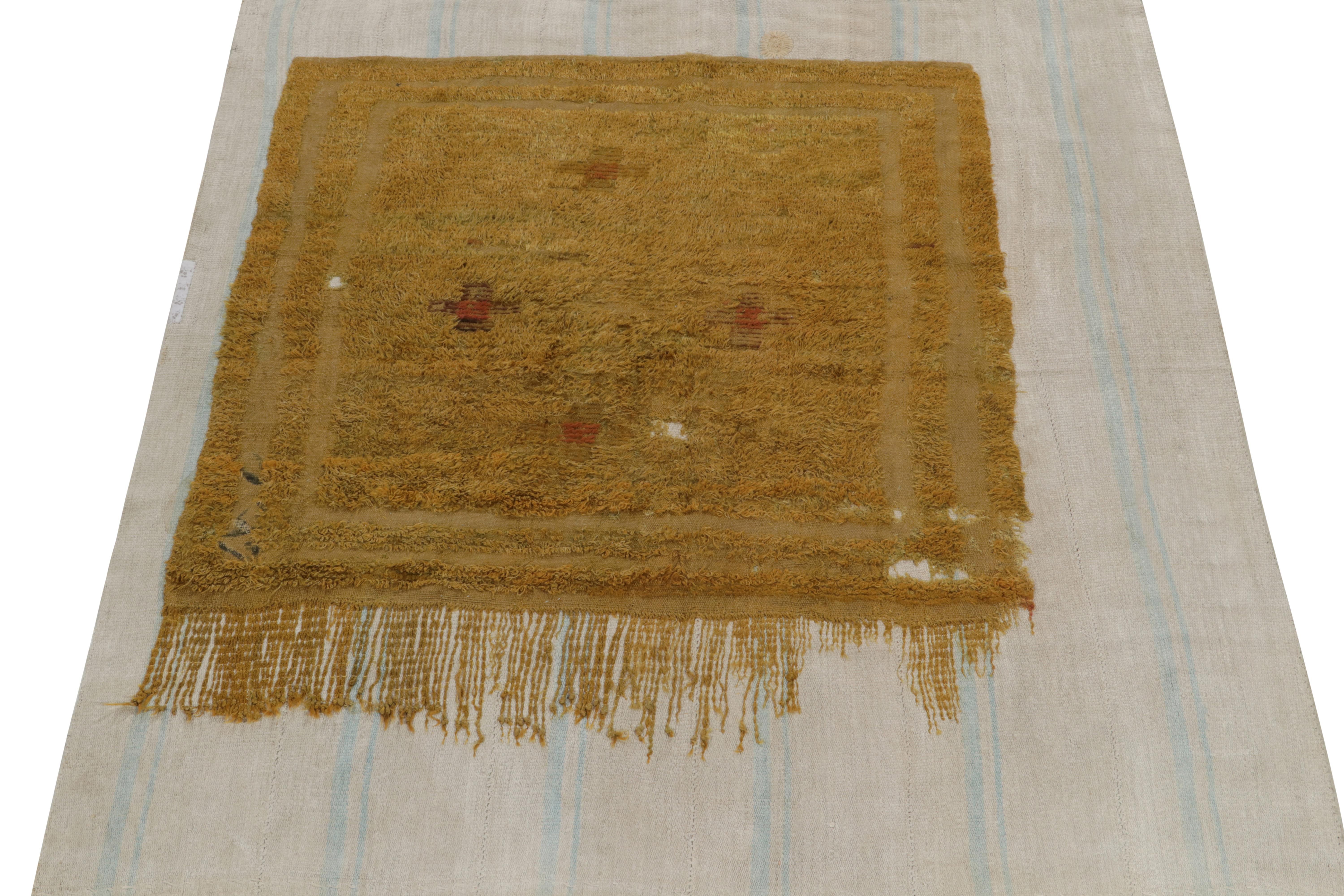 Handgeknüpft aus feiner Wolle, ein 5x6 Fragment Teppich mit distressed Ästhetik ruht ruhig auf einem blauen und grauen Flachgewebe. Das Fragment ist in üppigen Gold-Braun-Tönen gehalten, die ein natürliches Hoch-Tief auf dem Flachgewebe ergänzen -
