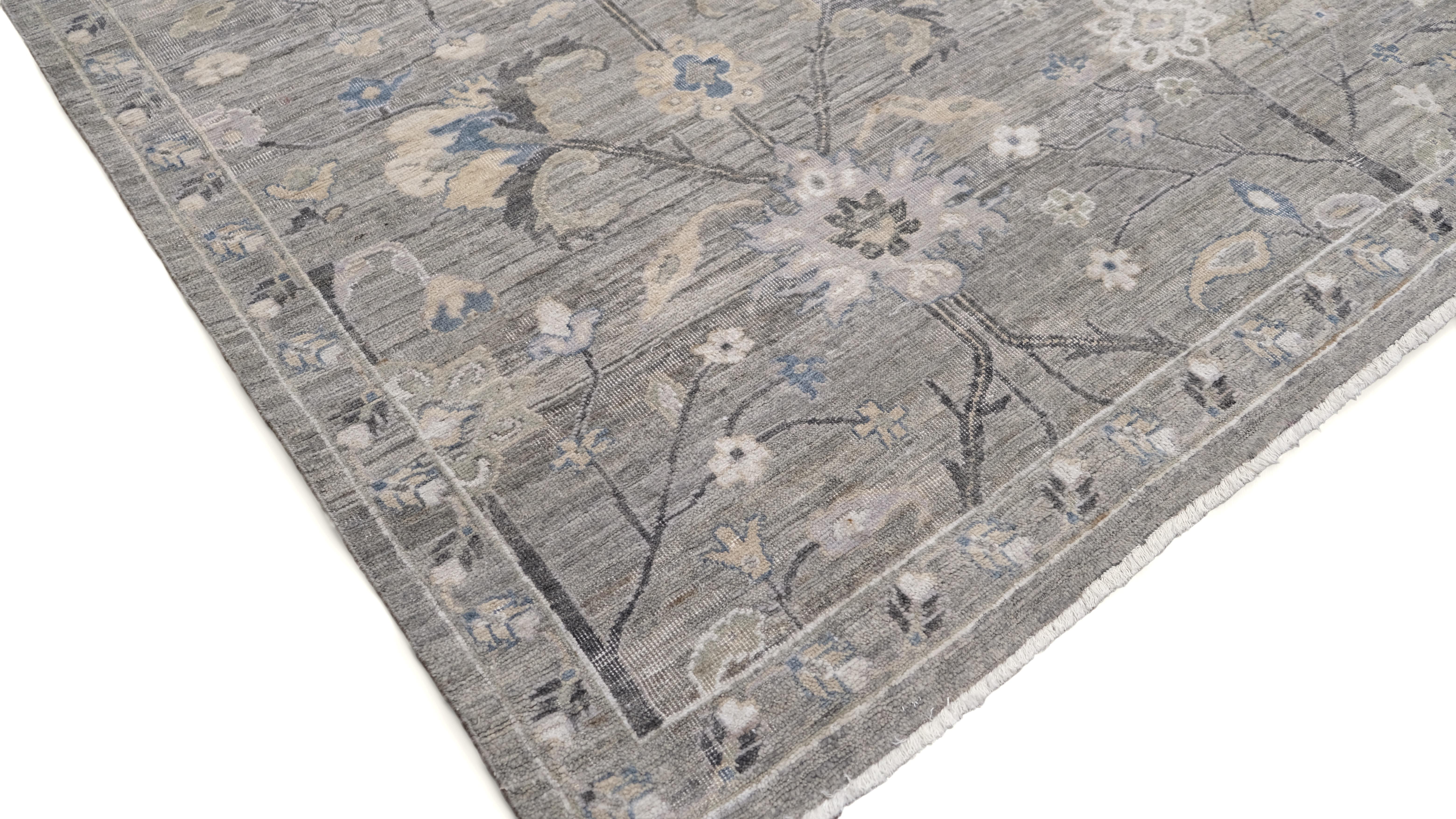 Dieser exquisite handgeknüpfte Wollteppich ist eine meisterhafte Mischung aus traditionellem Design und zeitgenössischer Eleganz. Ein zartes Blumenmotiv vor einem weichen grauen Hintergrund, akzentuiert mit dezenten Blau-, Creme- und Taupe-Tönen,