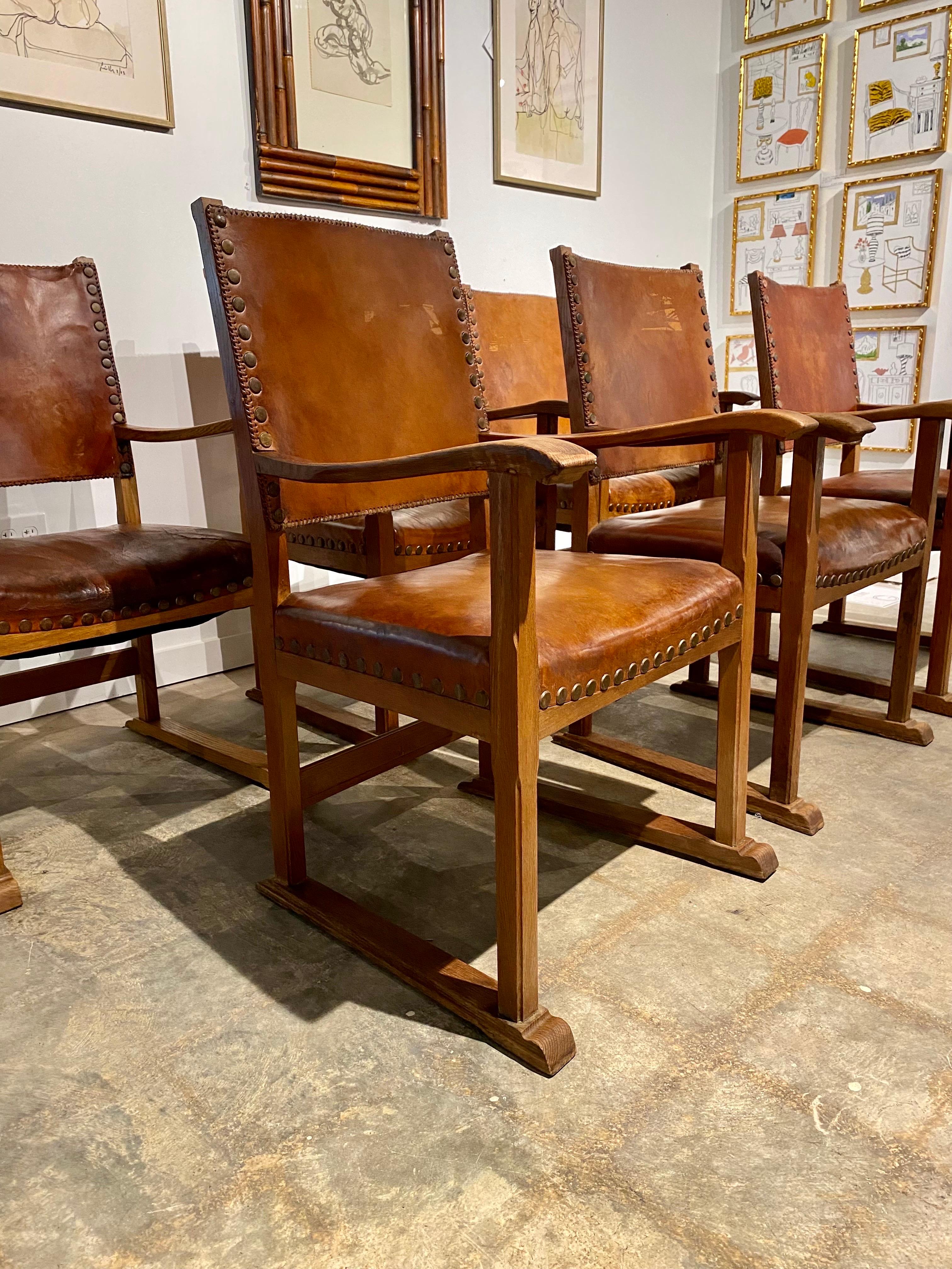 Unique sled base design with oak frames and heavy leather upholstery. Brass nailhead trim with carved oak frames. These show heavy wear but are usable as is. One of the seats is ripped through, however, as shown. An outstanding and eye-catching set