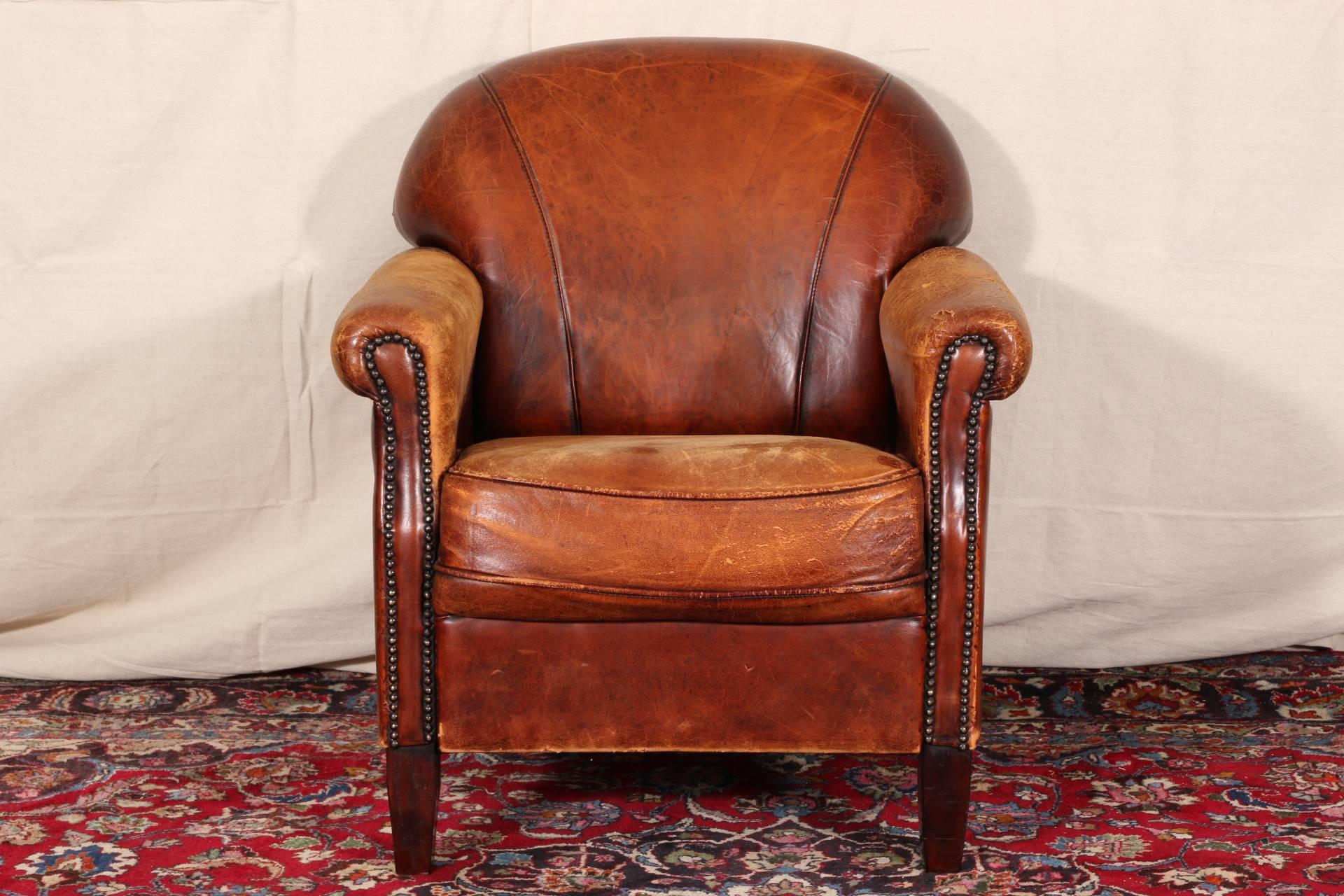 Distressed leather club chair, with a fan shaped back and tack details on the fronts of the arms. Raised on square mahogany legs. 

Condition: Expected wear and signs of use including worn seat and arms, small hole at end of one arm.