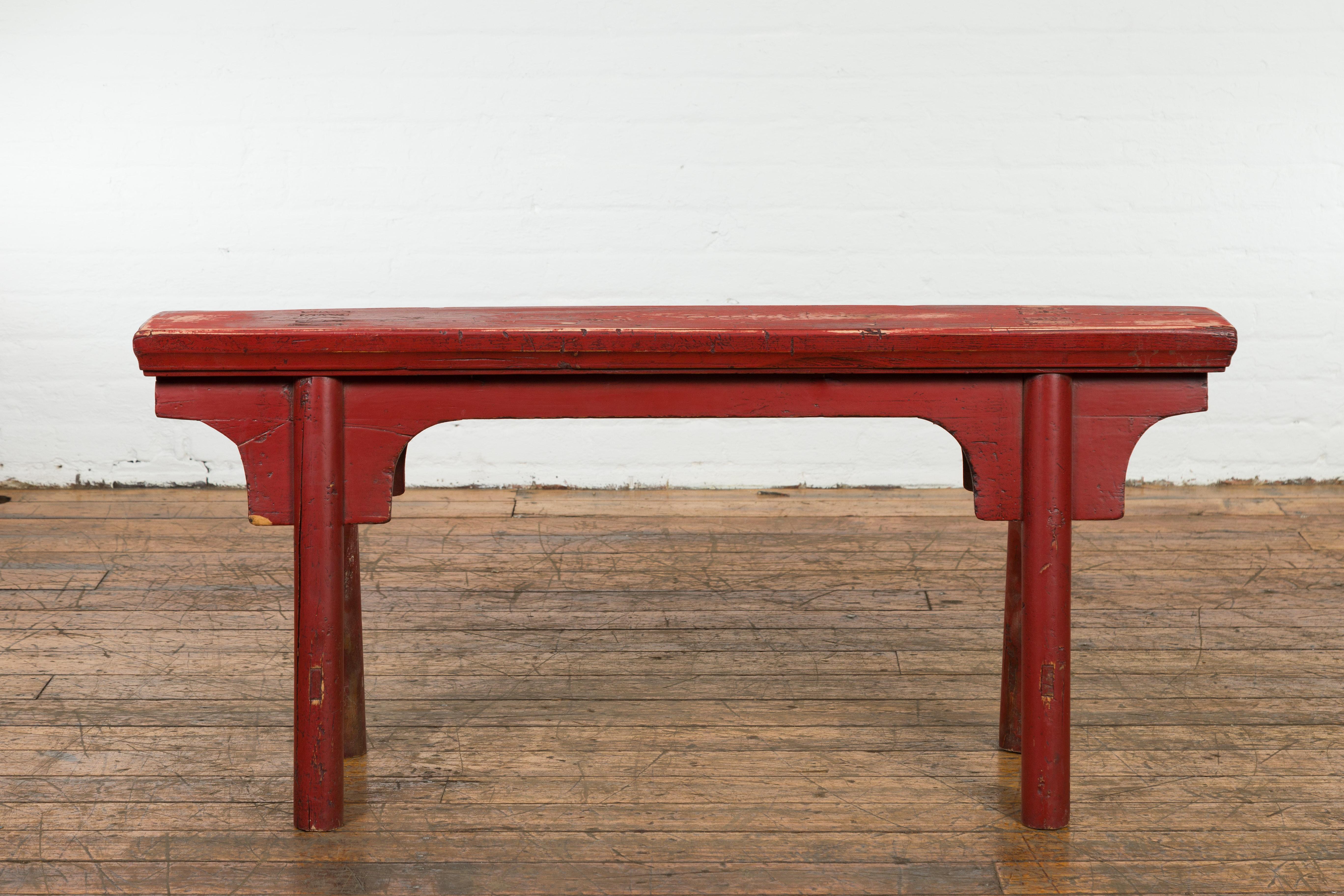 A Chinese vintage Ming Dynasty style red lacquer wooden bench from the mid 20th century with A-form base, carved spandrels and distressed finish. Exuding rustic elegance and simplicity, this vintage Ming Dynasty style red lacquer wooden bench from