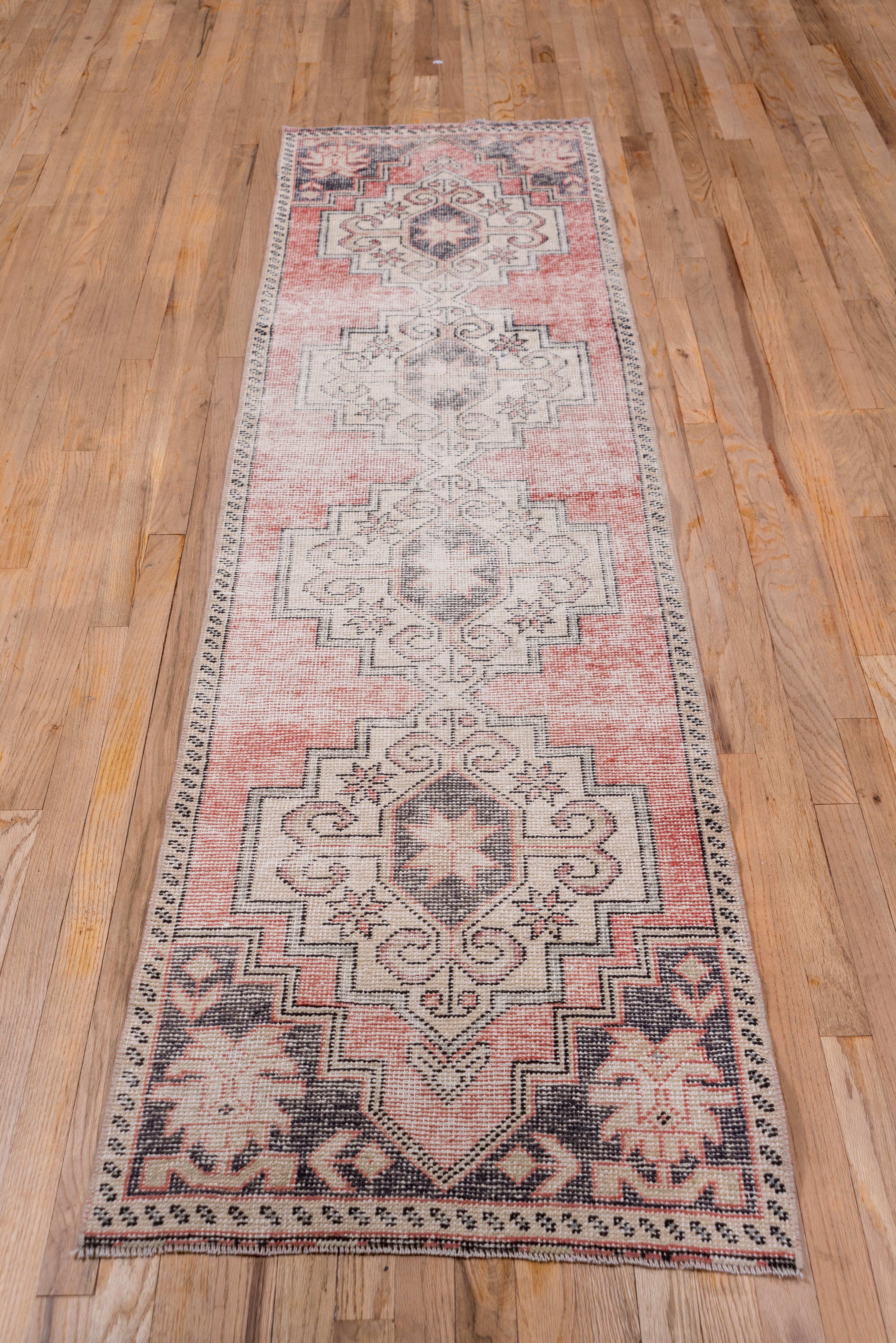 This small runner in distressed condition shows four large stepped sandy lozenges on a light, abrashed soft red ground within dark brown corners centered by ragged palmettes. The pattern is totally geometric with particularly bold rams' horn hooked
