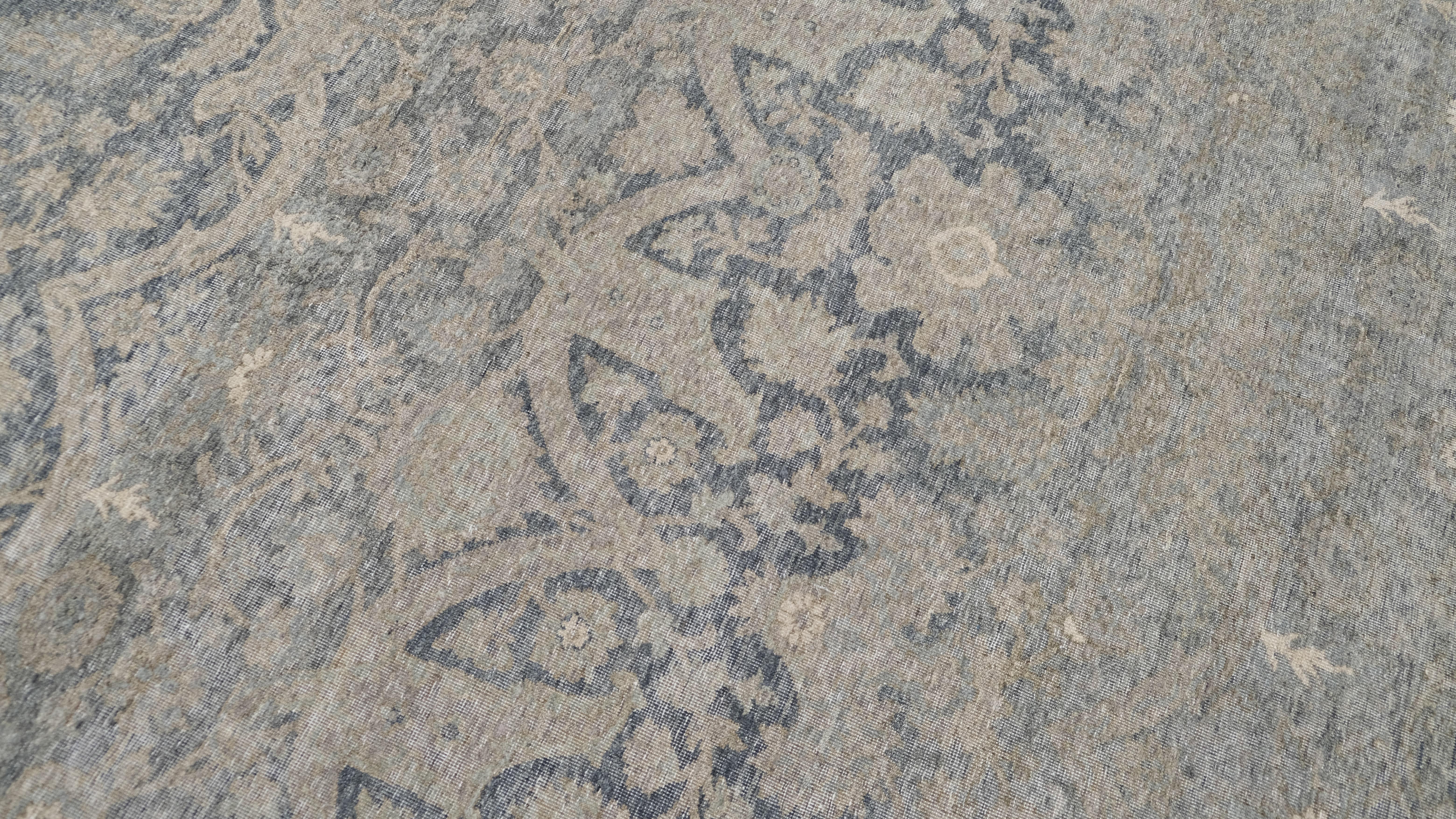 Ce tapis en laine noué à la main présente un design traditionnel sophistiqué et vieilli, avec un motif floral et des volutes complexes dans des tons gris doux et bleus sourds. Les subtiles variations de tons et les détails savamment délavés lui