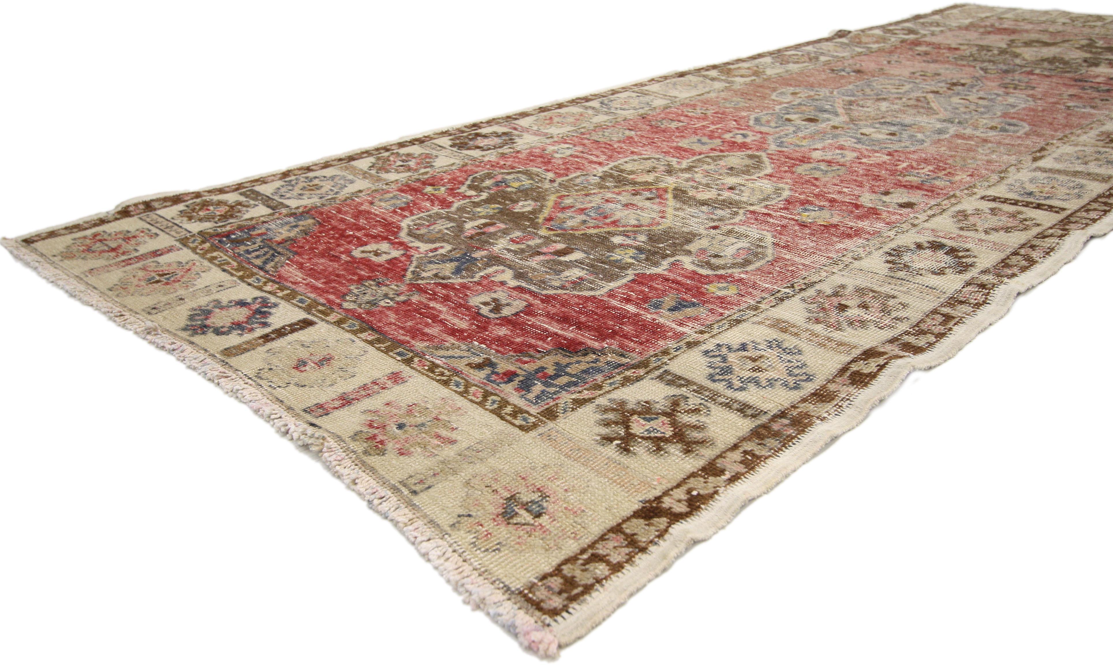 74675, distressed vintage Oushak runner. This distressed vintage Turkish Oushak runner features three central medallions in an abrashed red field surrounded by a geometric border. Rendered in variegated shades of red, rose, coffee, sienna, navy