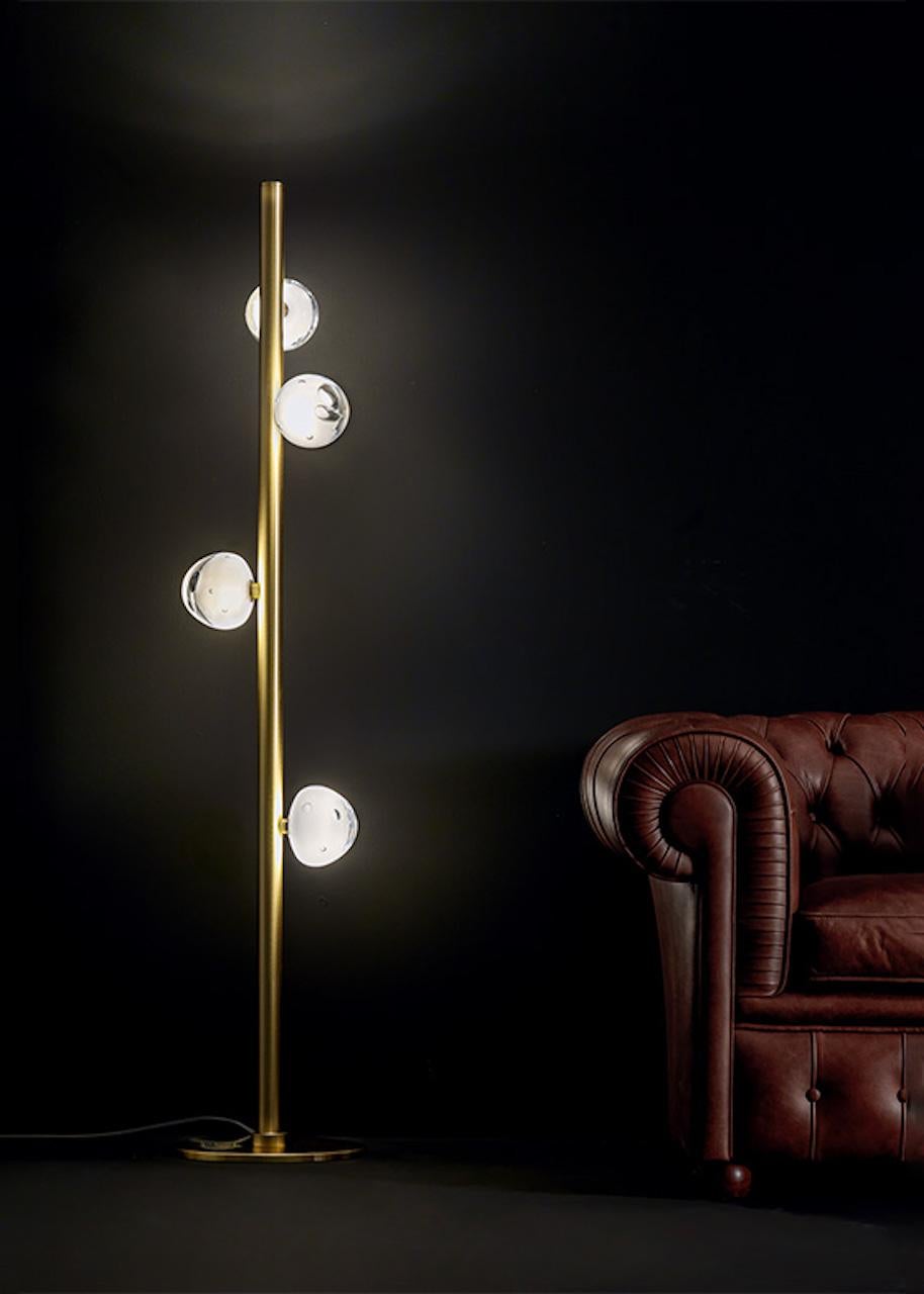 Floor lamp with cylindrical structure in satin-finish brass, and crystals made by hand. The light source is placed at the upper end of the lamp to emit a direct beam.