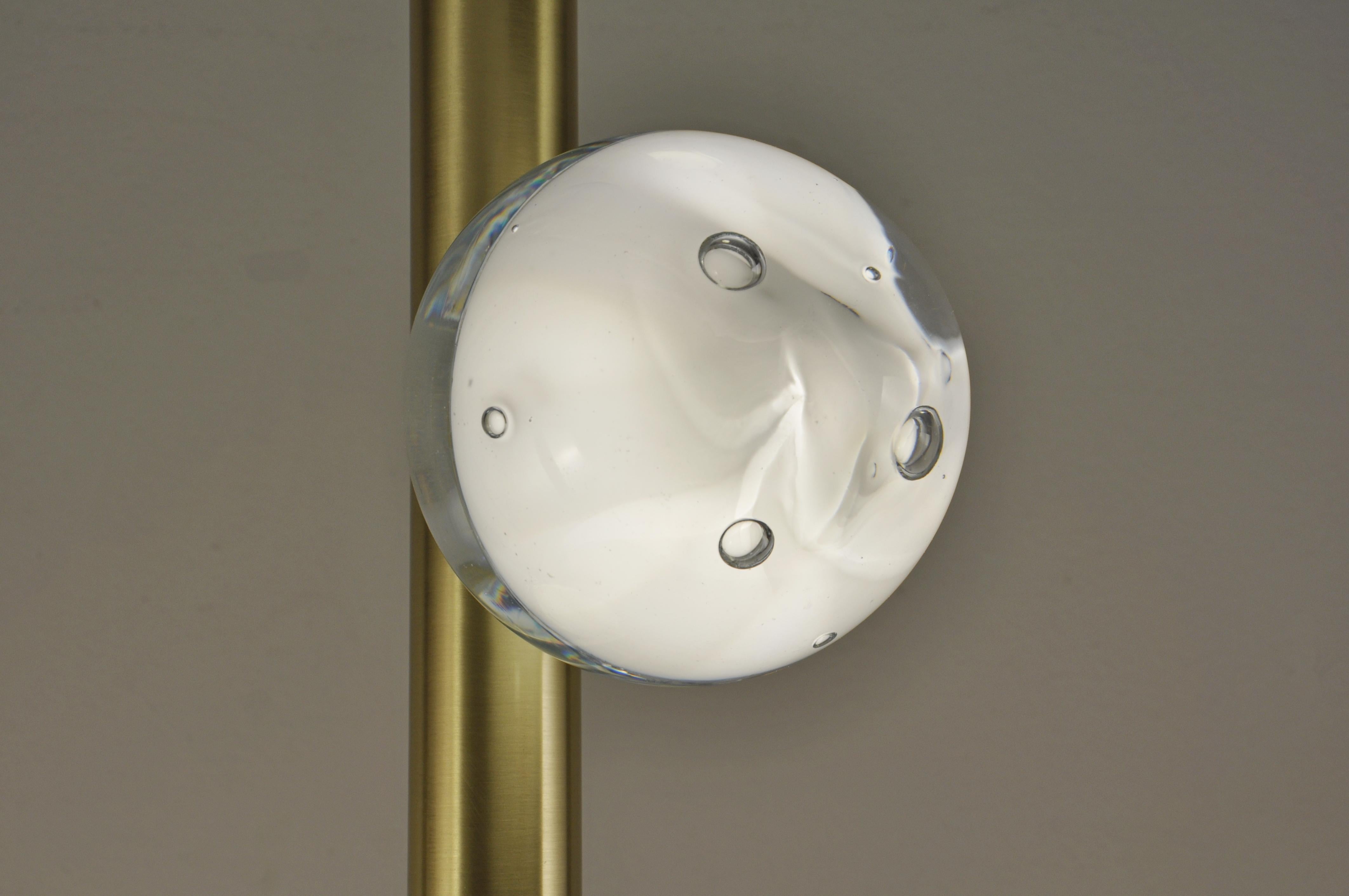 Suspension lamp with cylindrical structure in satin-finish brass, and crystals made by hand to contain the light source. Beams of direct light are emitted at the two extremities.