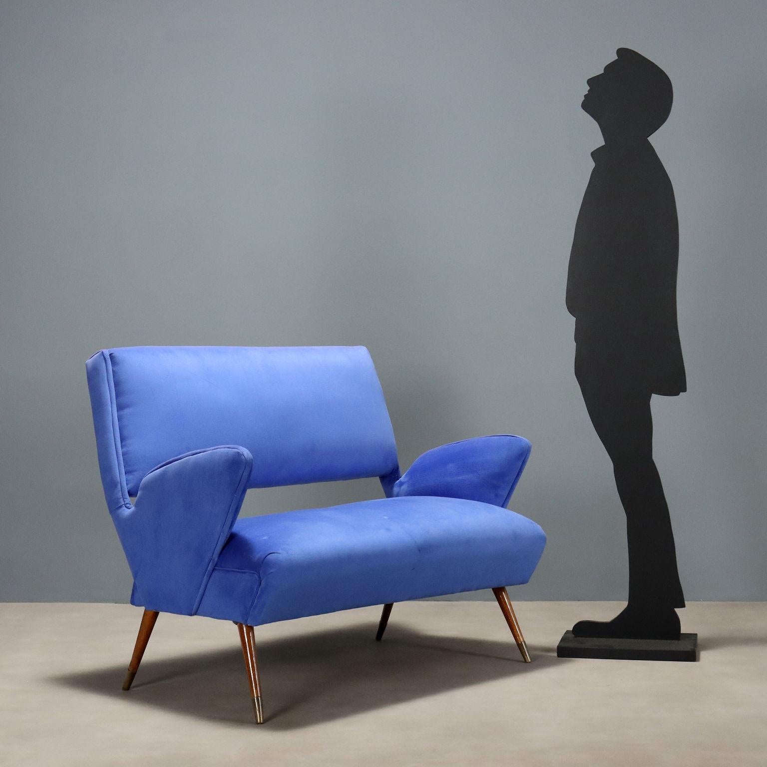 Divanetto vintage a due posti con braccioli dalla linea tondeggiante, imbottito in espanso e rivestito in velluto bluette. Divano dalla forma molto particolare che può essere rinnovato nella tappezzeria scegliendo tra le varie proposte presenti nei
