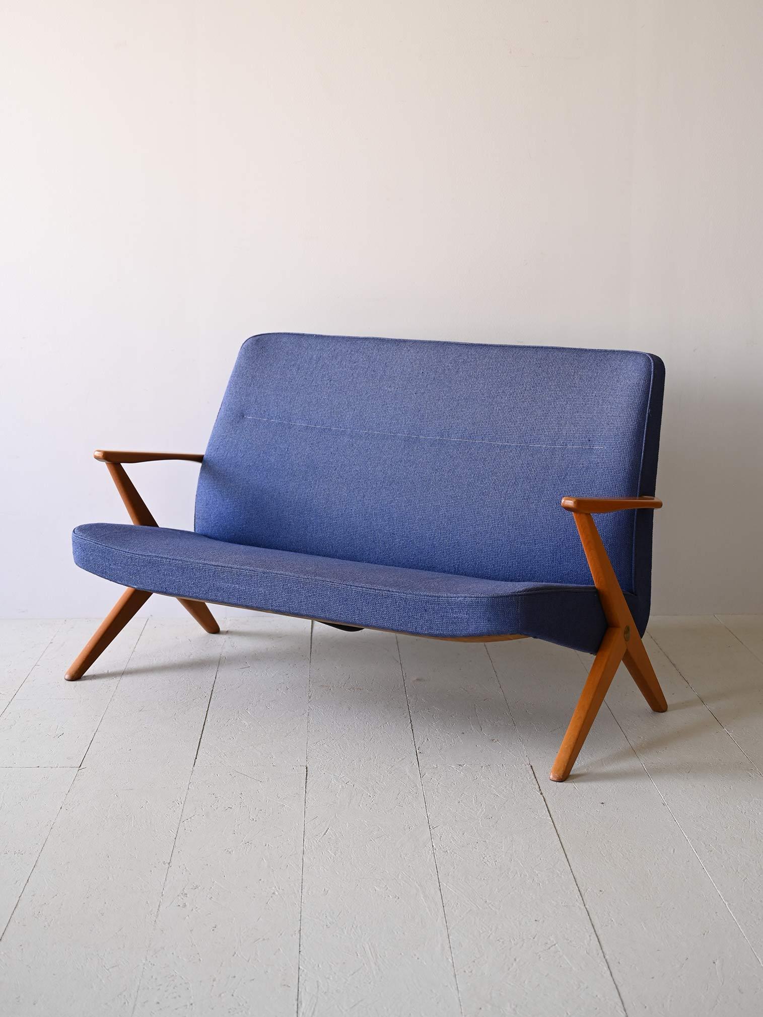 Nordic sofa in original vintage blue fabric.

Designed by Bengt Ruda for NK in the 1950s, it was manufactured in Sweden.
X-shaped legs offer stability and modernity, while rounded wooden arms add a touch of warmth and sophistication.

Its minimal