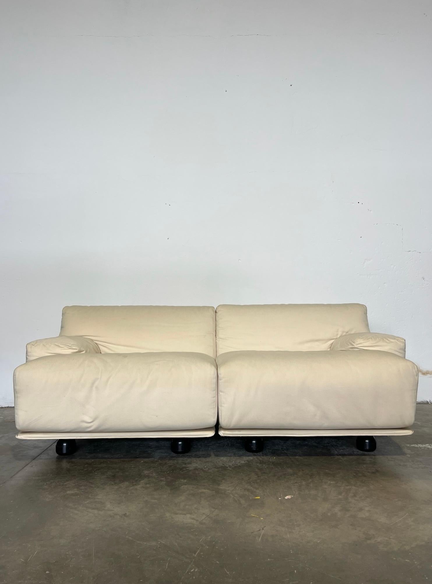 Magnífico diván Fiandra de dos plazas, diseñado por Vico Magistretti para Cassina en los años 70, en excelentes condiciones vintage. Revestido en tejido blanco panna, emana elegancia y refinamiento, perfecto para ambientes sofisticos. La estructura