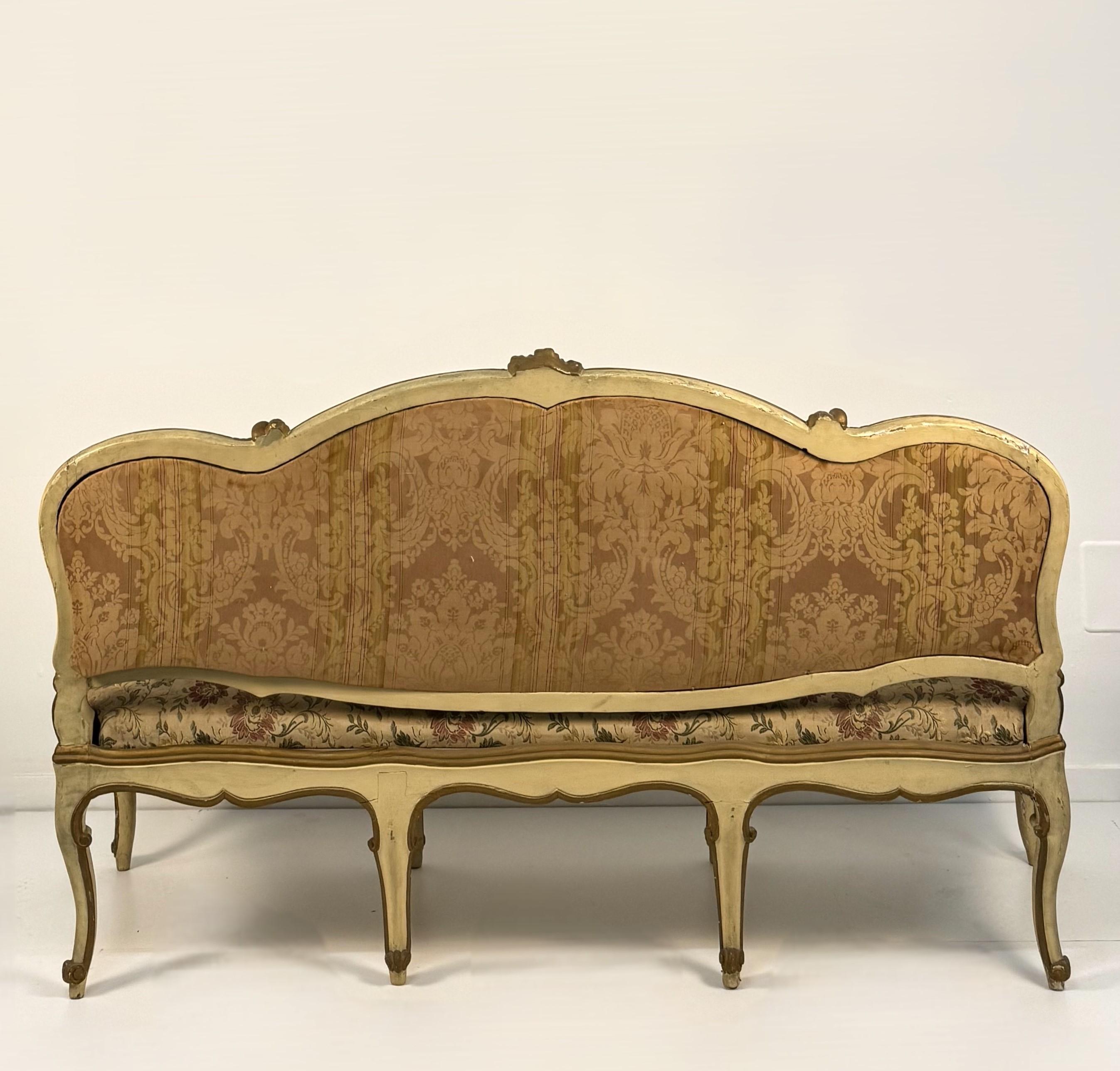 Lacquered and gilded wooden sofa, Lombardy, 18th century, shaped profiles decorated with gilded frames interspersed with rocaille motifs and small scrolls, upholstered arms on shaped uprights, carved belt on arched legs, toe foot, polychrome