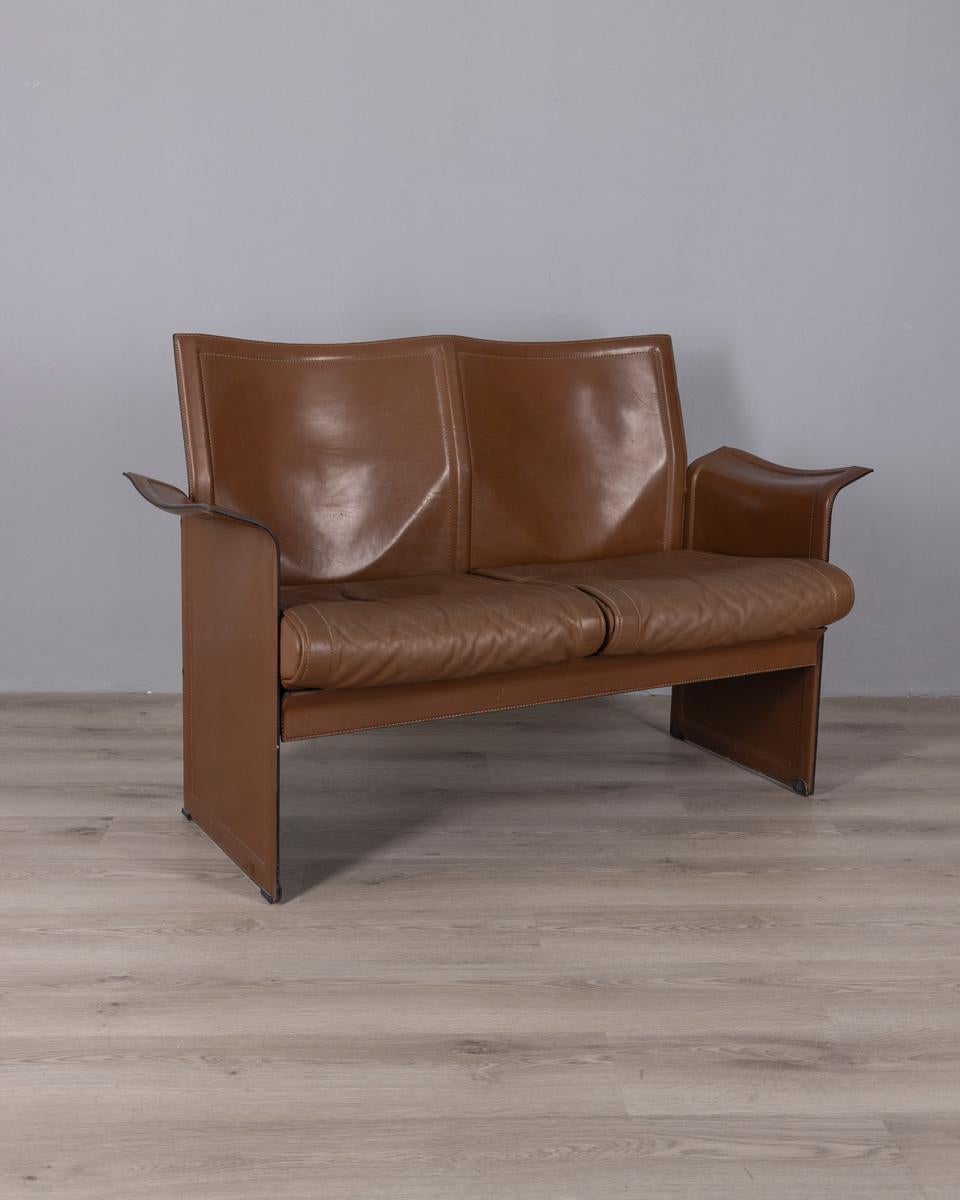 Brown leather two-seater sofa, 'Korium' model designed by Tito Agnoli for Matteo Grassi, 1970s.

CONDITION:
In good condition, with signs of wear due to time.

SIZING:
Height 83 cm; width 130 cm; depth 55 cm;

MATERIALS:
Metal and leather.

YEAR