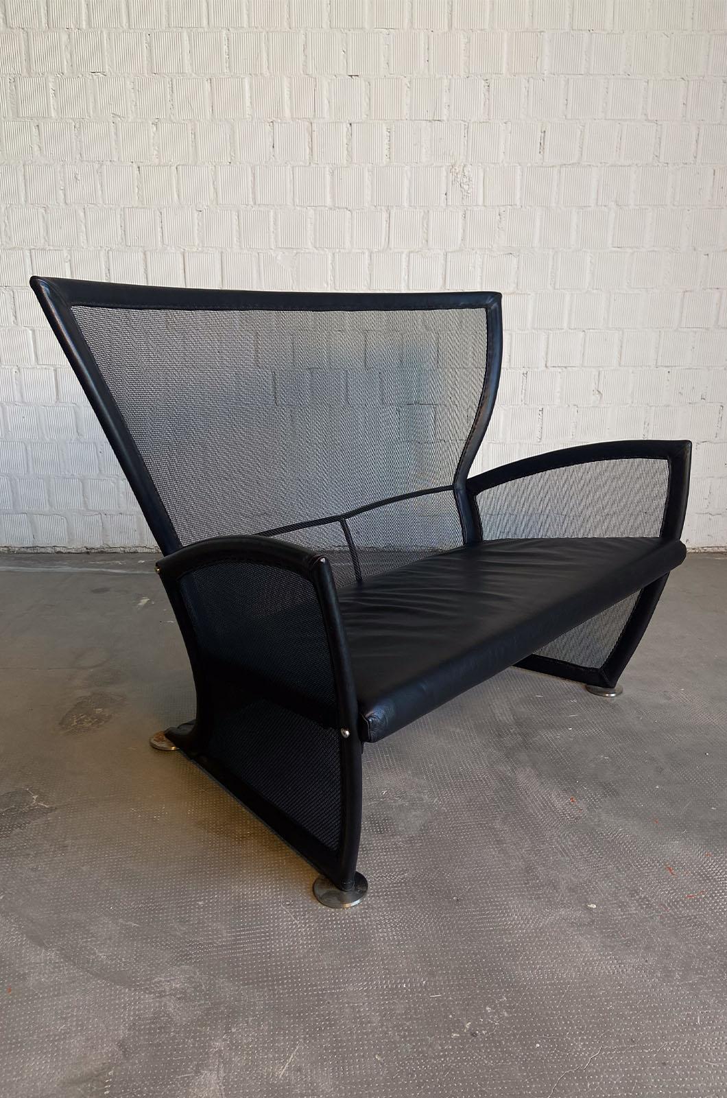 Canapé Privè conçu par Paolo Nava pour Arflex en 1987. La structure du canapé est constituée d'une maille et d'un tube en aluminium recouvert de cuir noir. Les accoudoirs sont en plastique, tandis que l'assise et les coussins sont encastrés et