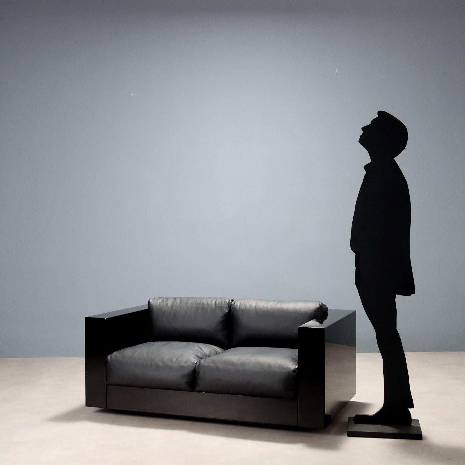 Canapé deux places avec structure en bois laqué noir, coussins en mousse et revêtement en cuir noir. La marque du fabricant 