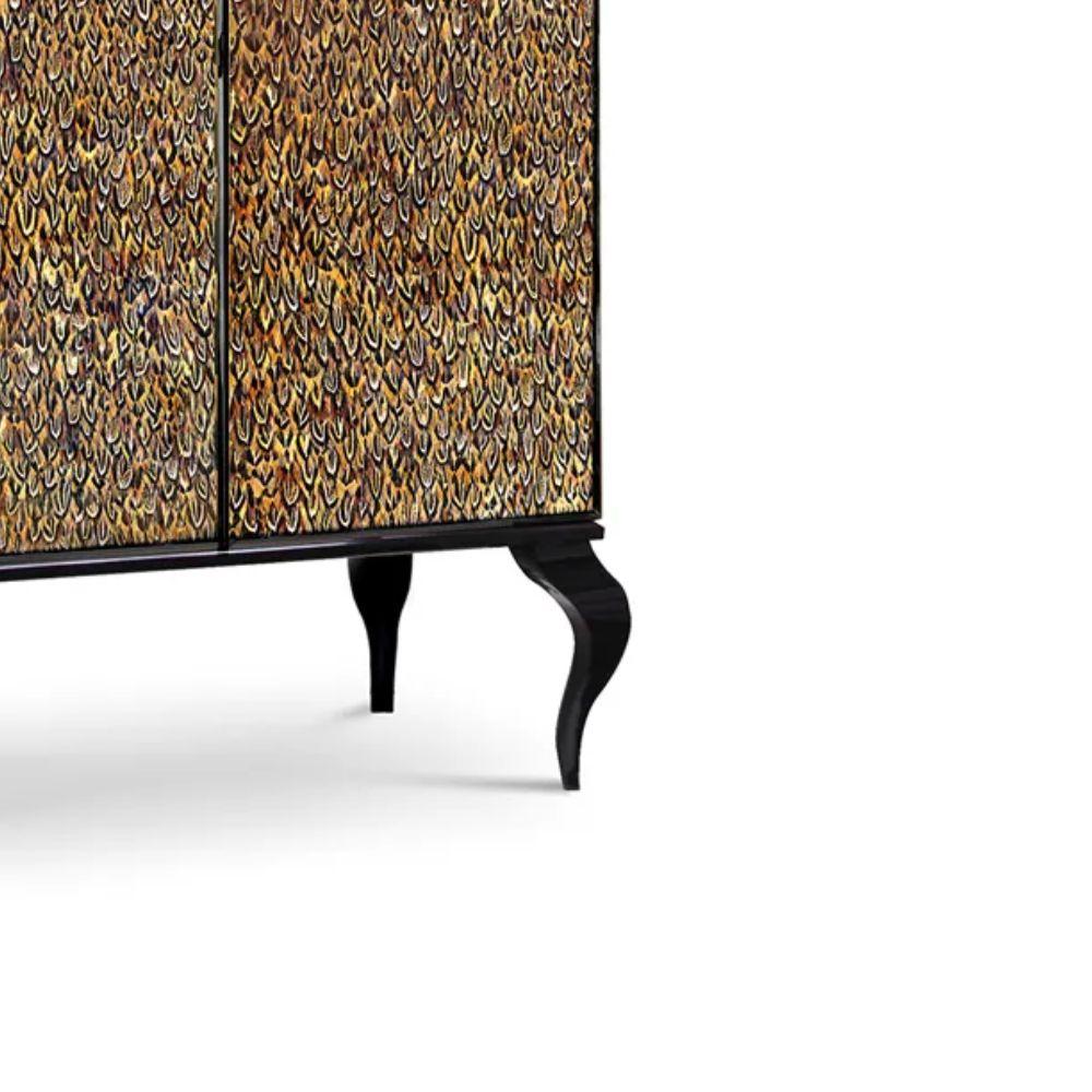 Questo armoire a doppia anta con piano a pagoda è ricoperto di delicate piume naturali posizionate singolarmente. Uno squisito nastro metallico apre le porte a un interno sontuoso impreziosito da quattro cassetti e due ripiani regolabili. Il piano e