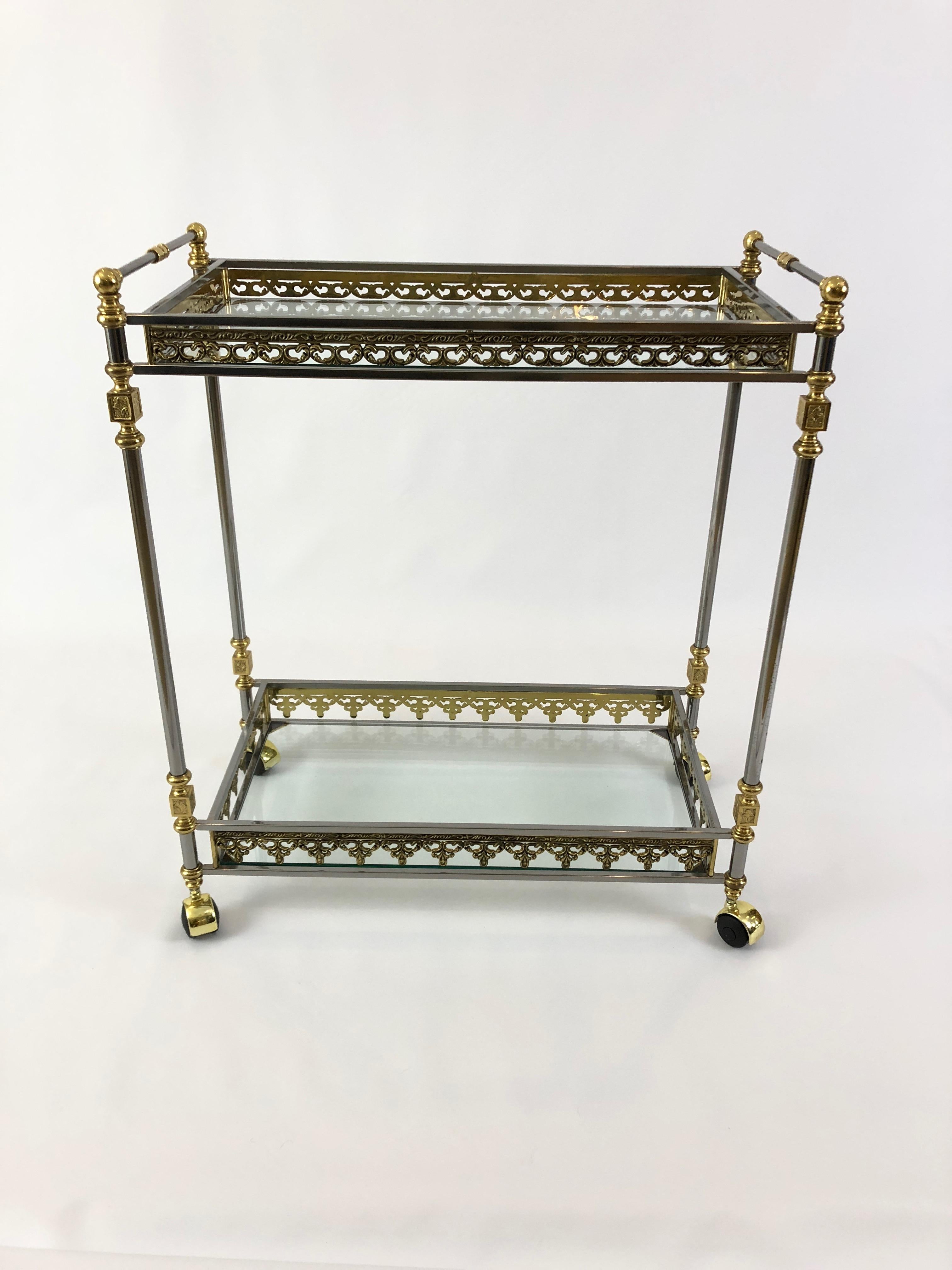 An unusually beautiful two-tier bar cart having an intricately decorative mix of brass and nickel with 2 glass shelves. Even the wheels are elegantly capped with brass. A rare find.