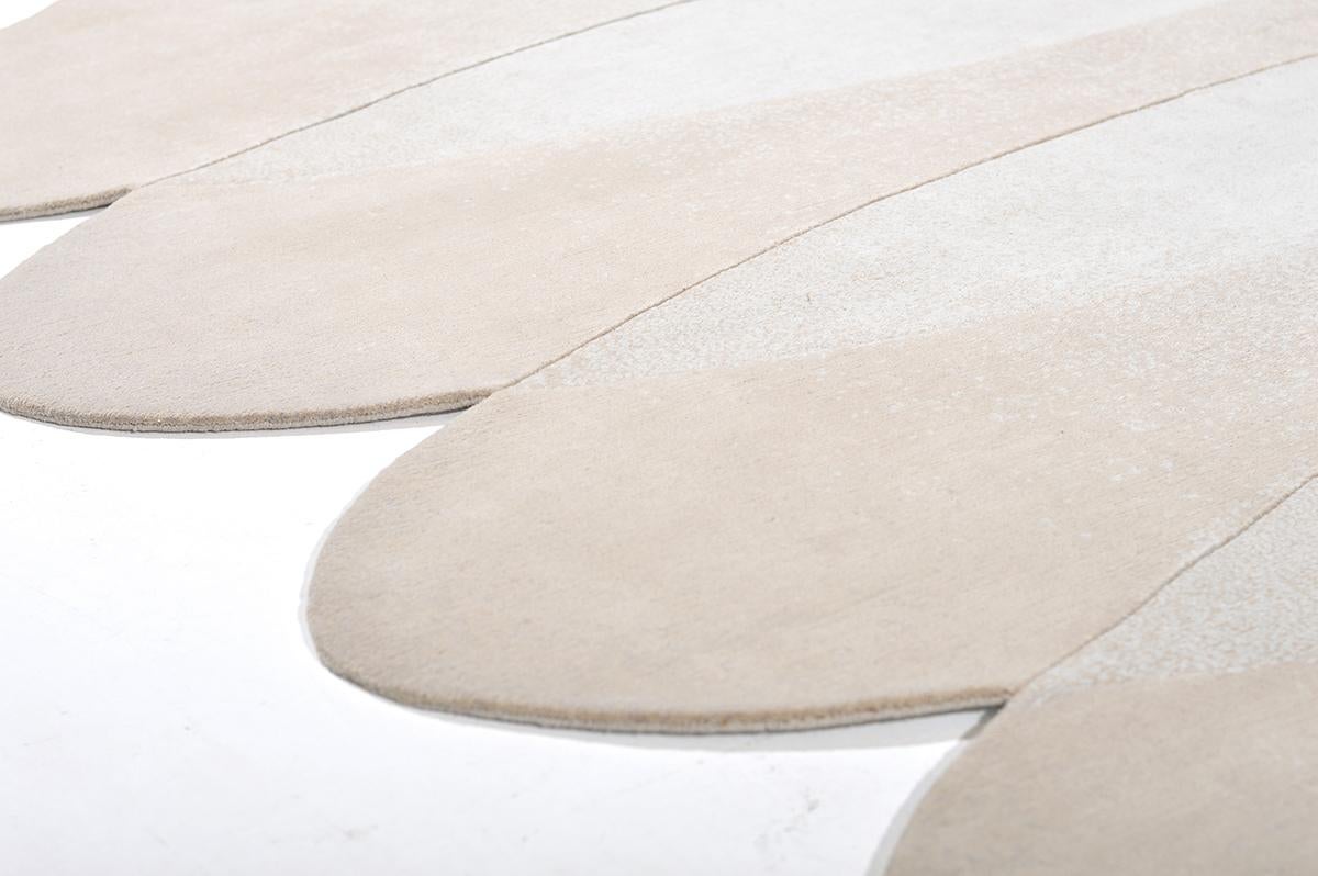 Modern abstract shapes and a sophisticated use of color come together to create this luxurious wool and silk hand woven shaped rug. Warm neutral tones and a repetition of shapes allow this rug to have a soft elegant presence or premier as a