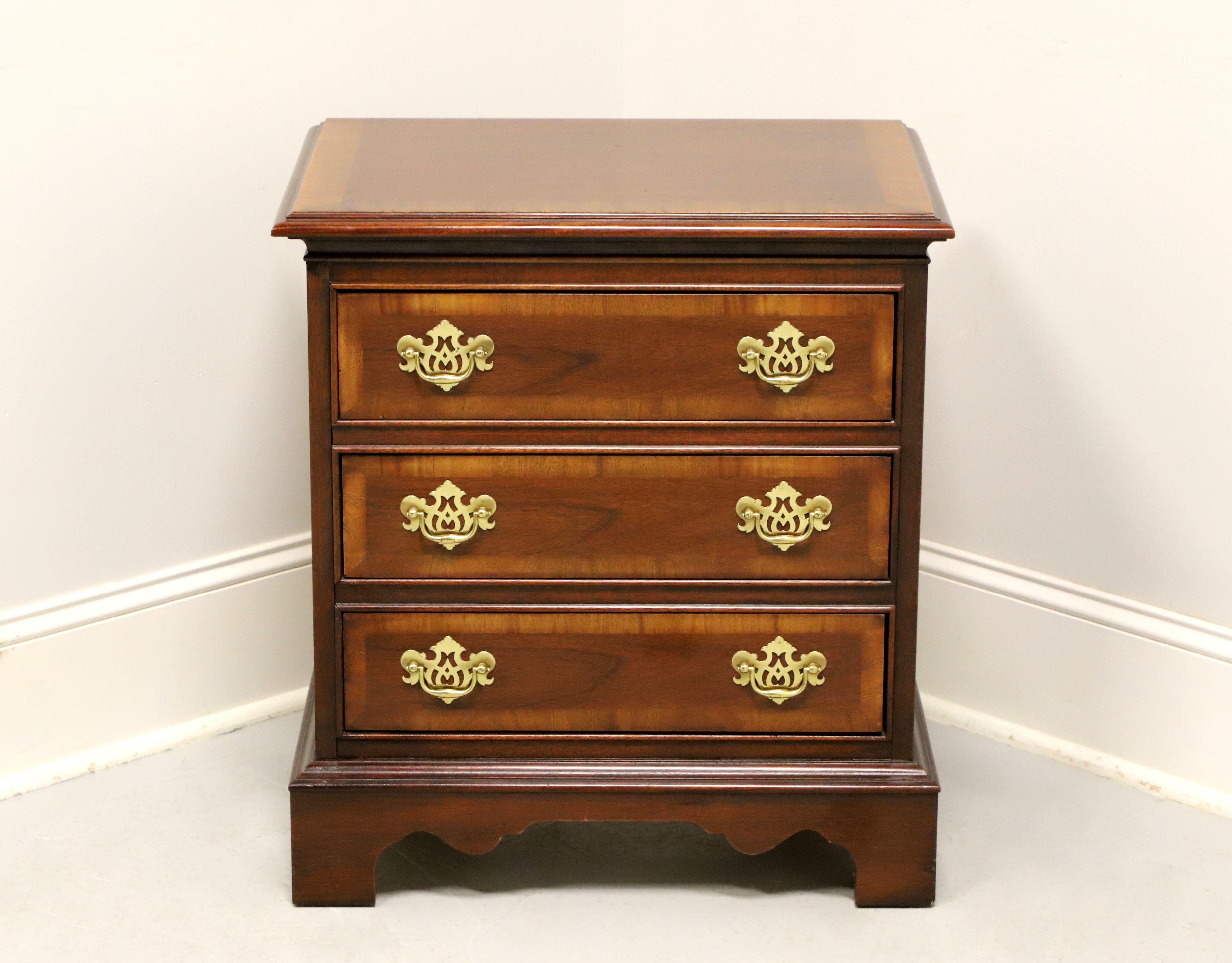 A Chippendale style bedside chest by Dixie Furniture. Mahogany with brass hardware, banded inlaid top with bevel edge, banded drawer fronts, and bracket feet. Features three drawers of dovetail construction. Made in Lenoir, North Carolina, USA, in