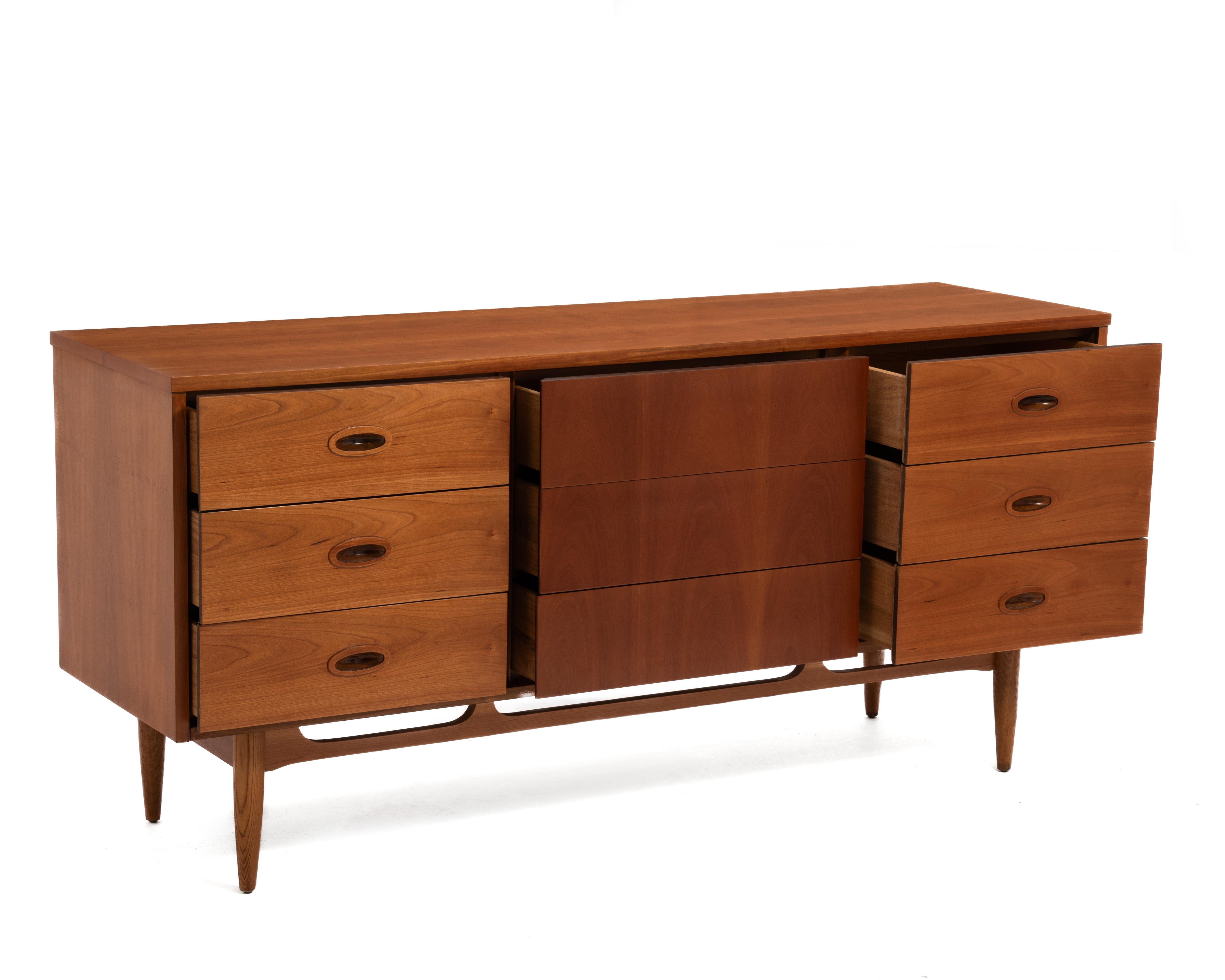 A Mid Century dresser by Dixie Furniture. The dresser has nine drawers, the six outside drawers have inset pull handles and the center drawers have hidden handles. Made with cherry veneer with solid legs. The dresser has been professionally