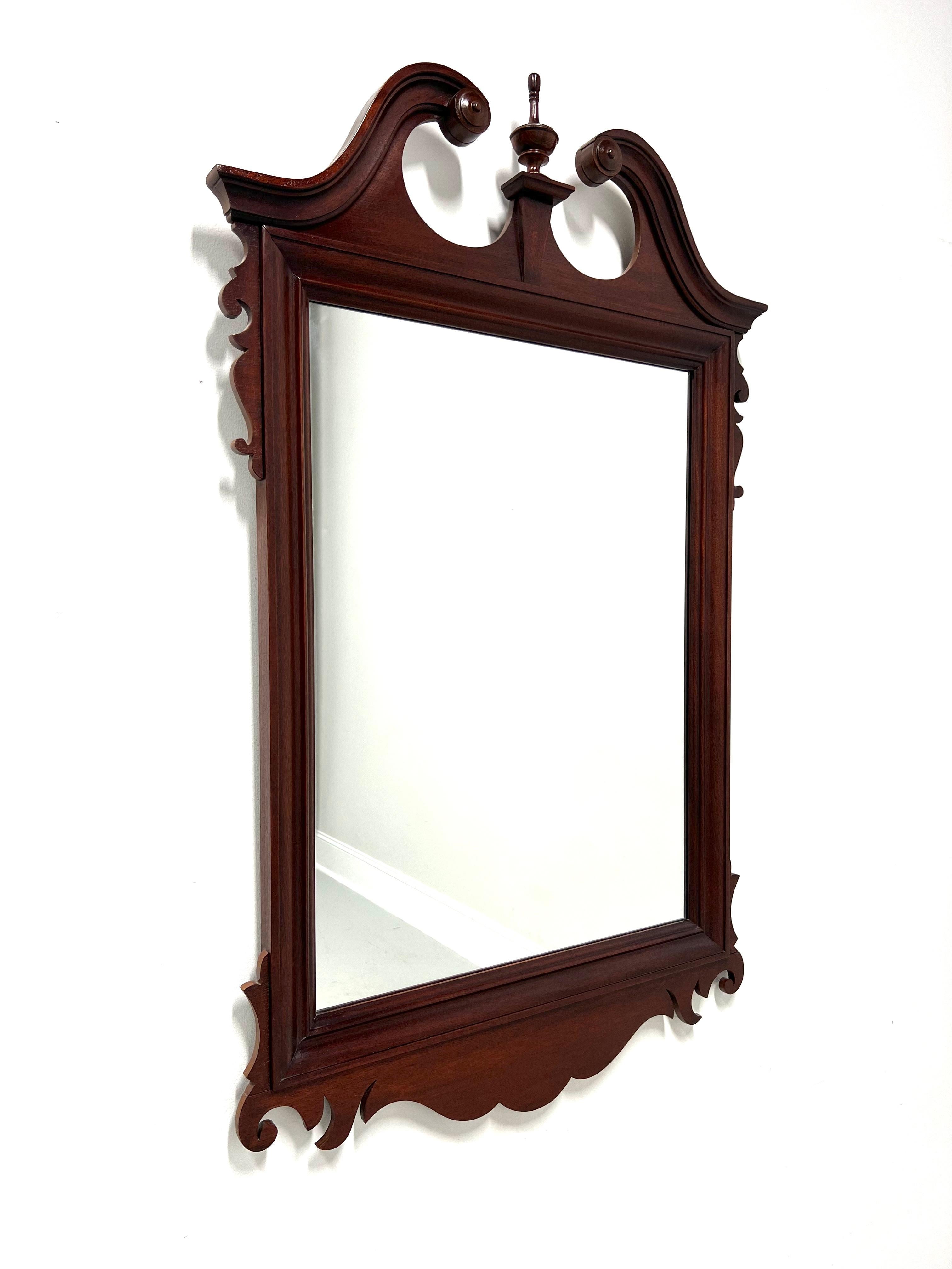 A Chippendale style wall mirror by Dixie Furniture. Mirrored glass in a mahogany frame with pediment top, a center finial, and decorative carvings at top sides & at the bottom. Made in Lenoir, North Carolina, USA, in the late 20th Century.

Style #: