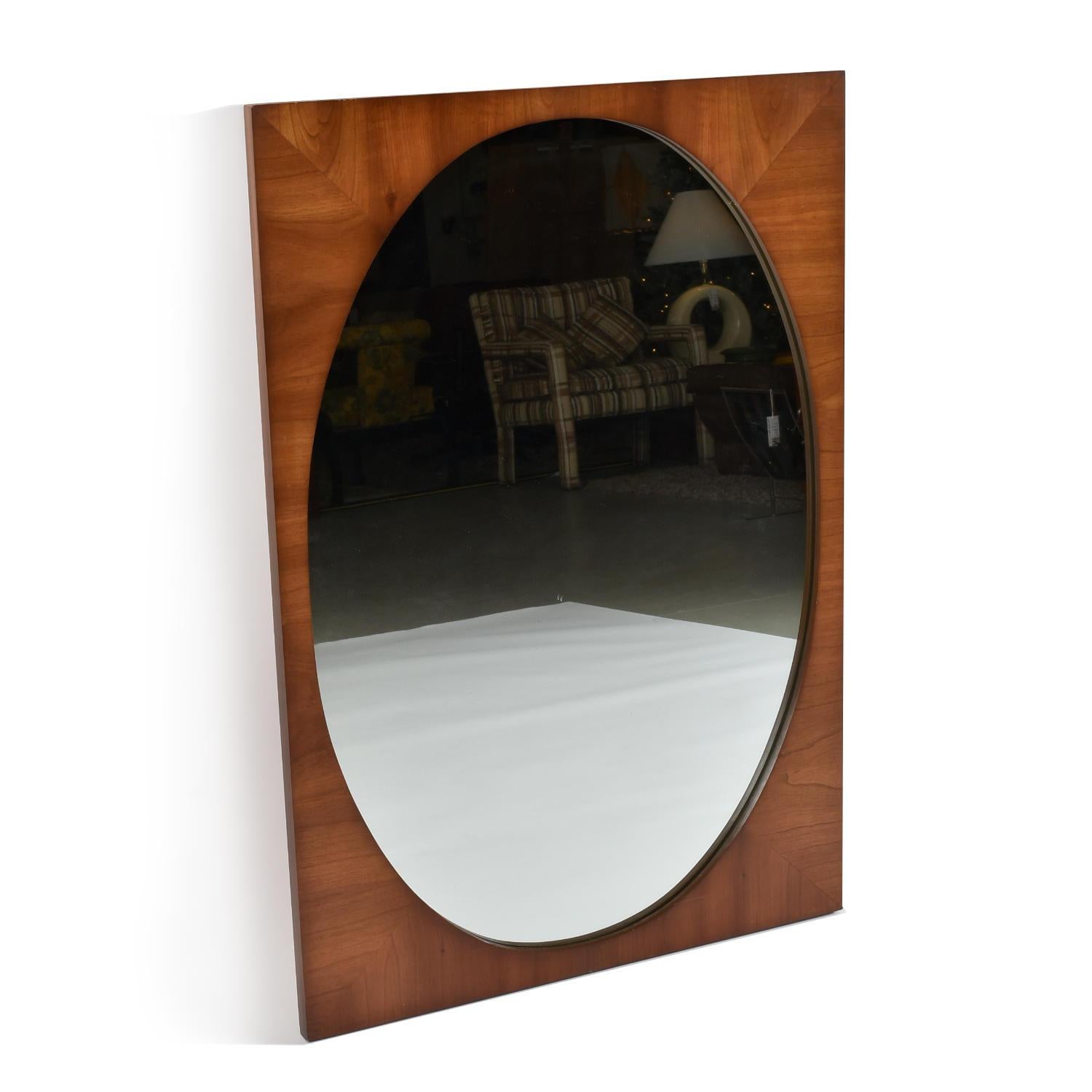 Handsome Mid-Century Modern walnut wall mirror by Dixie. The exceptional mirror has book matched walnut veneer, evidenced in each of the four corners. The vertically oriented piece is rectangular with inset, oval mirror glass. A new French cleat is