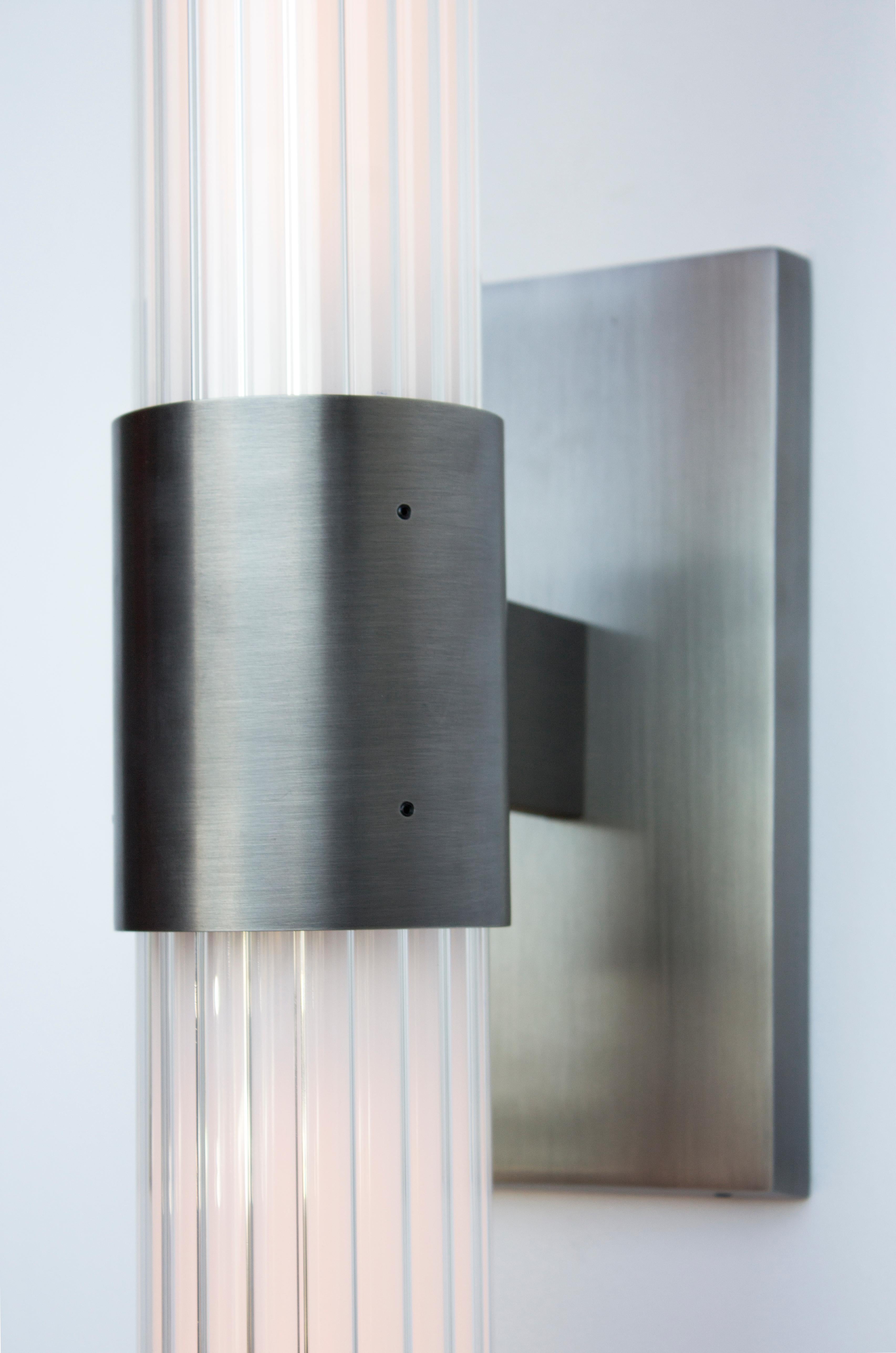 The Dixie series centers around a bold fluted glass light assembly. The Dixie Sconce puts this detail on display at a gently leaning angle with its wall mounted brass brace available in multiple finishes.

LAMPING:
(2) 5W E-26 LED Tubular T9 Bulbs,