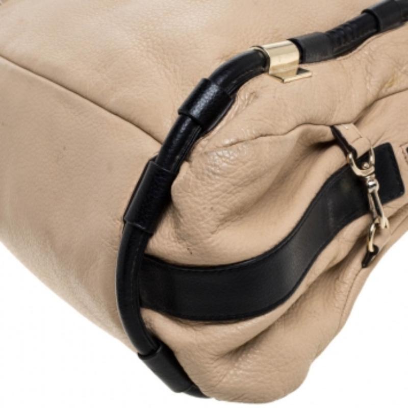 Grab this DKNY bag and deliver chic looks every day. Crafted from beige & black leather, it has a lovely metal detailing in gold-tone hardware, logo charm. dual handles and a spacious fabric-lined interior with a zip closure. It is a must-have!